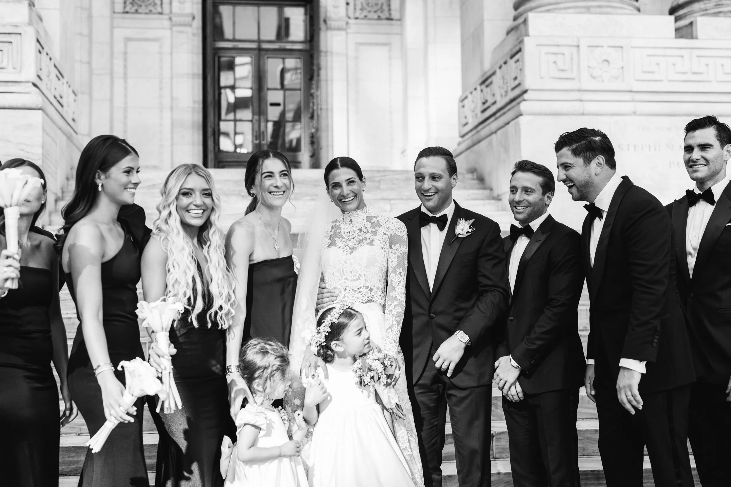 Black and white group portrait of the full wedding party on the steps of the New York Public Library, NYC wedding