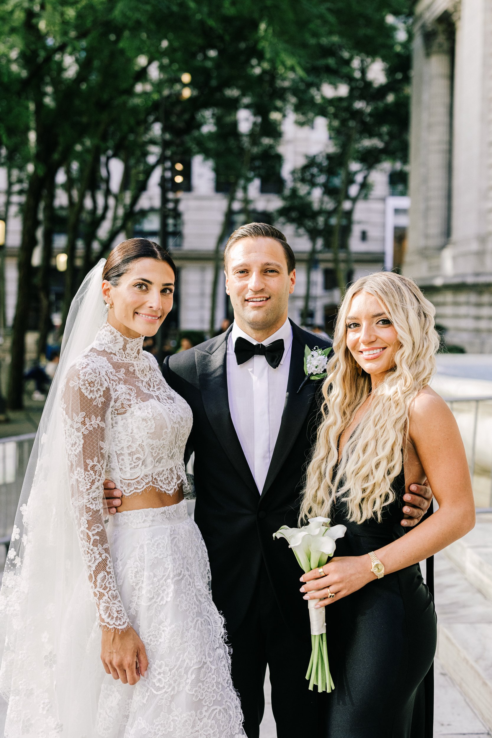 Bride and groom smiling with a bridesmaid in a candid outdoor portrait near the New York Public Library, NYC wedding