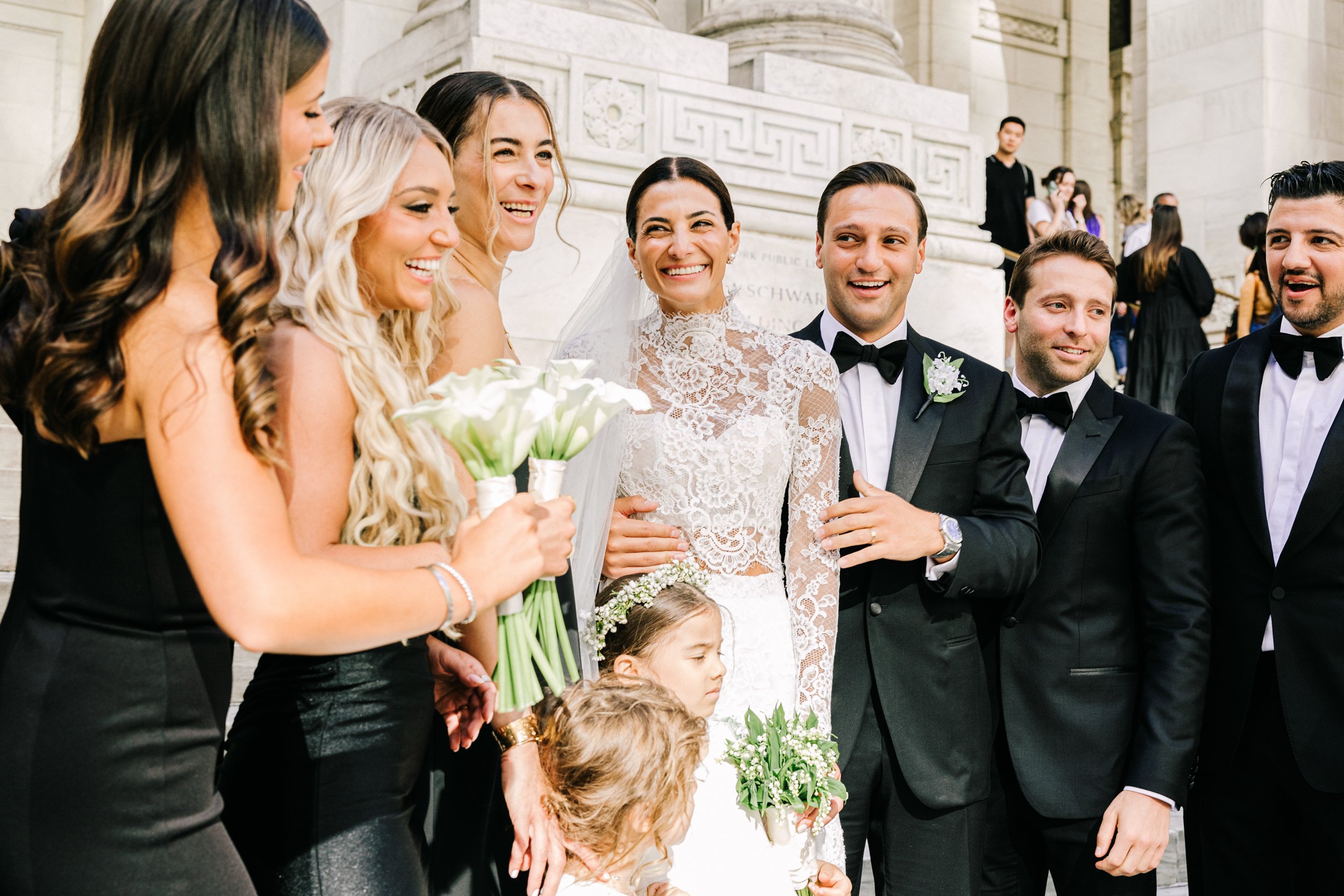 Candid joyful moment with the bride, groom, bridesmaids, and flower girl laughing together at the New York Public Library, NYC wedding