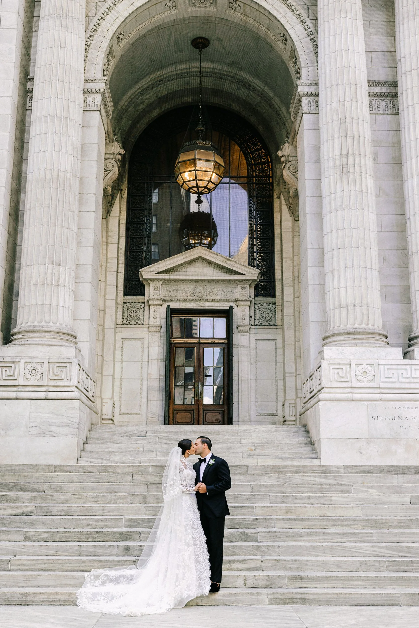 Bride and groom standing beneath the grand arched entrance of the New York Public Library, showcasing the iconic architecture, NYC wedding