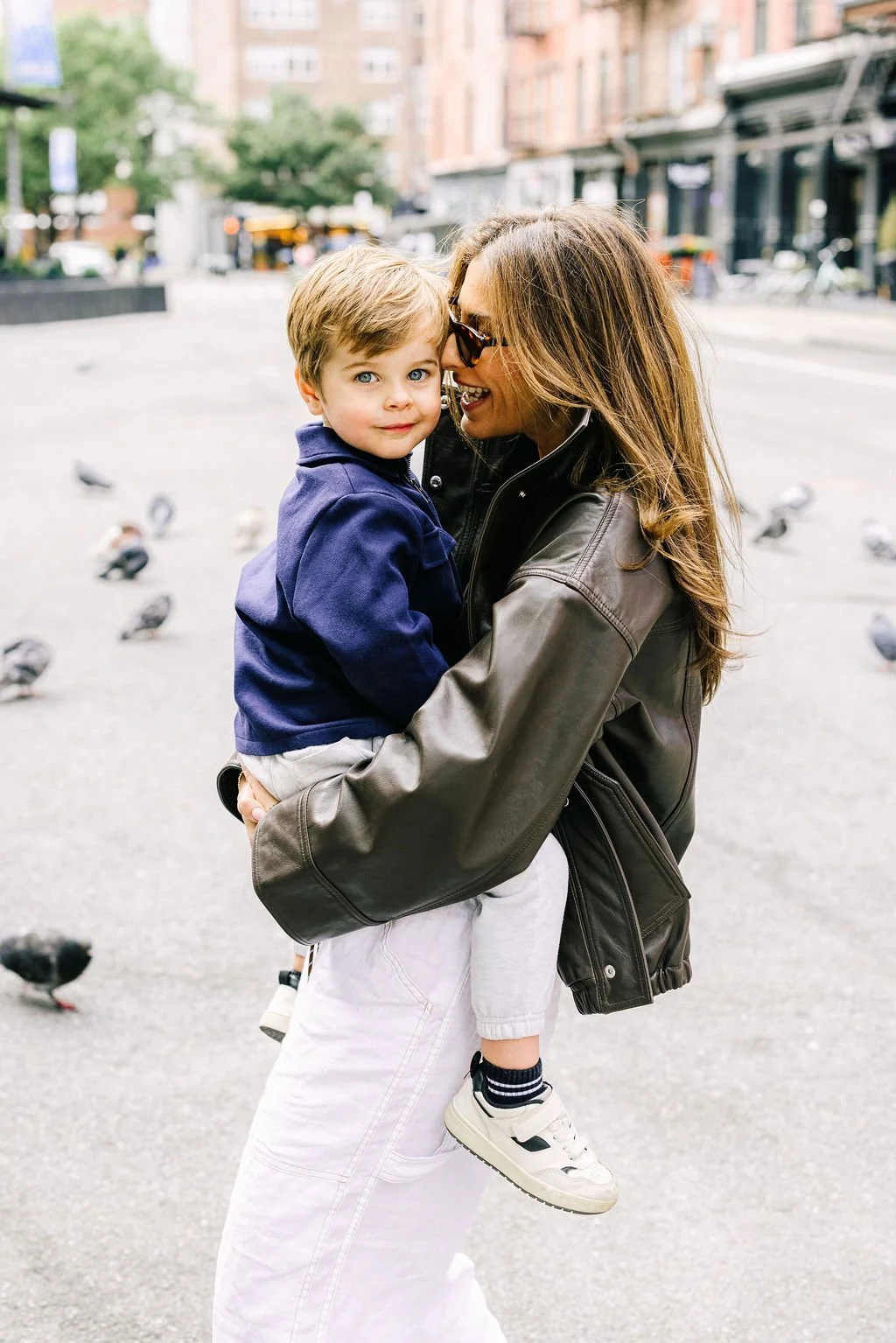 Mother holding her son during a family portrait session in New York City with pigeons and a yellow cab in the background