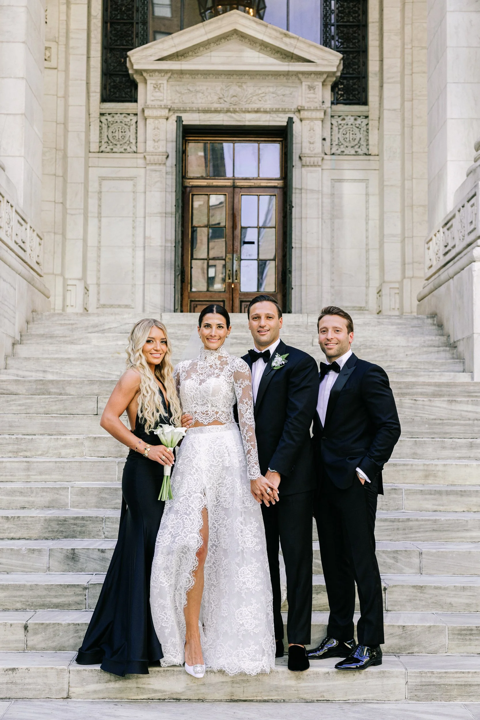 Bride and groom posing with a bridesmaid in a black gown on the steps of the New York Public Library, NYC wedding