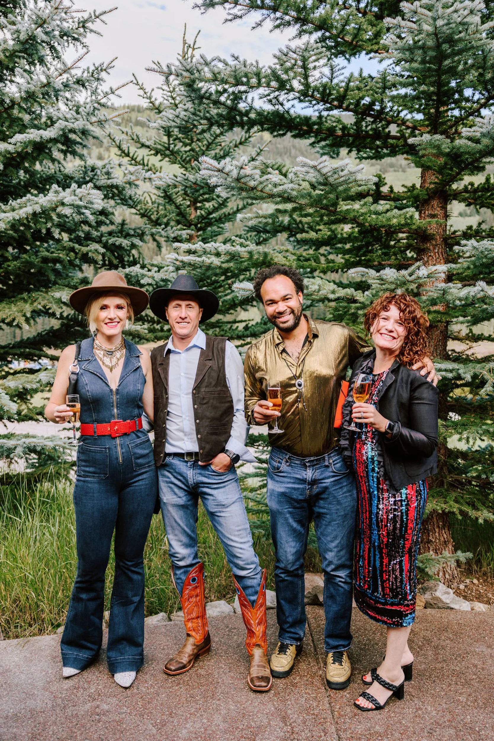 Wedding guests dressed in western rodeo outfits posing in front of pine trees at Pine Creek Cookhouse wedding in Aspen Colorado