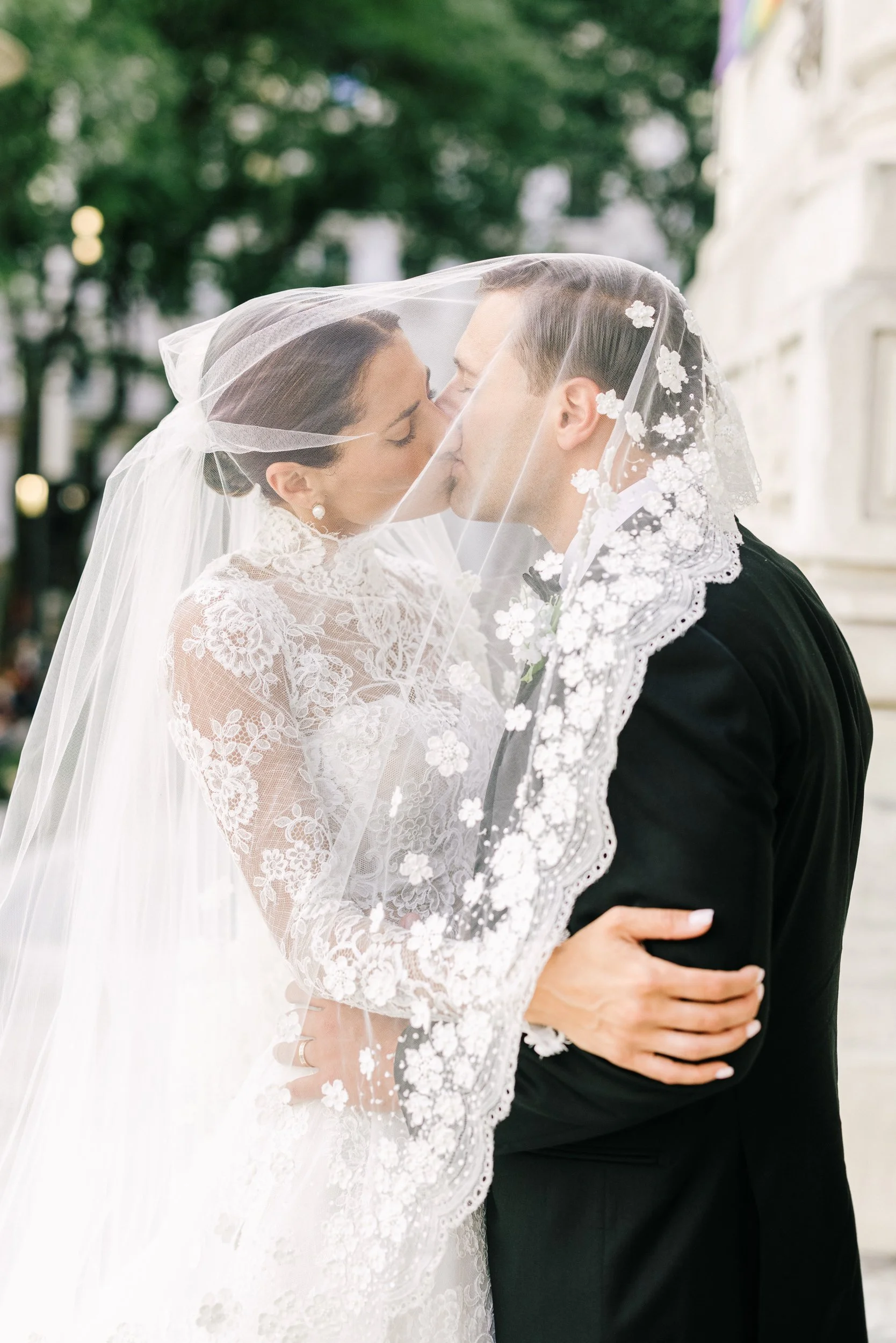 Romantic outdoor portrait of bride and groom sharing a kiss beneath the bride's flowing lace veil, New York Public Library wedding