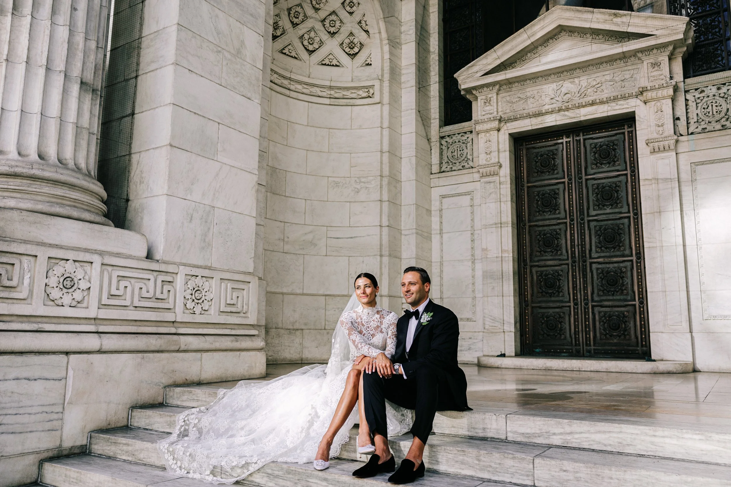Bride and groom seated at the base of the grand columns on the exterior steps of the New York Public Library, NYC wedding