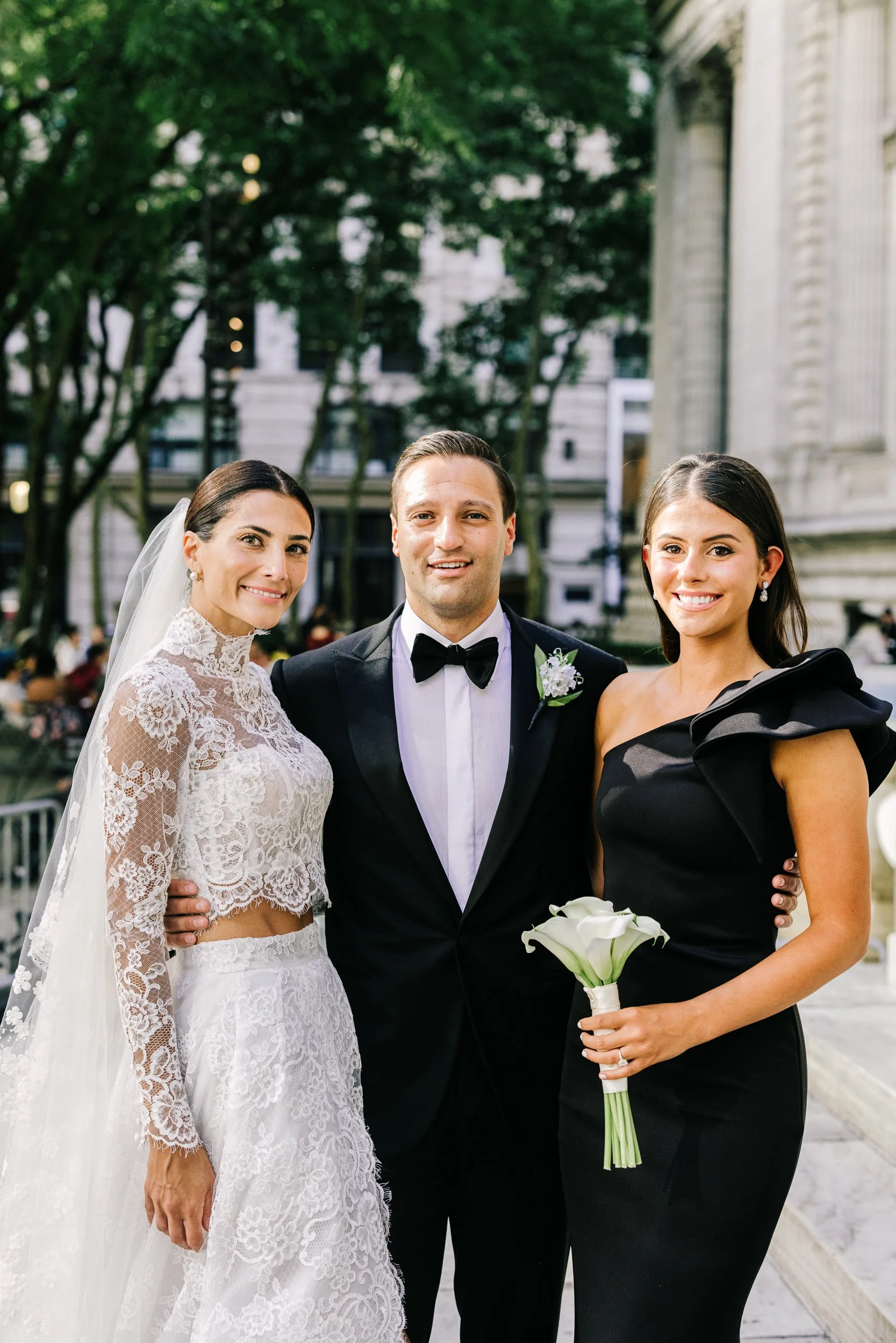 Bride and groom with a bridesmaid in a black off-shoulder gown in an outdoor portrait near the New York Public Library, NYC wedding