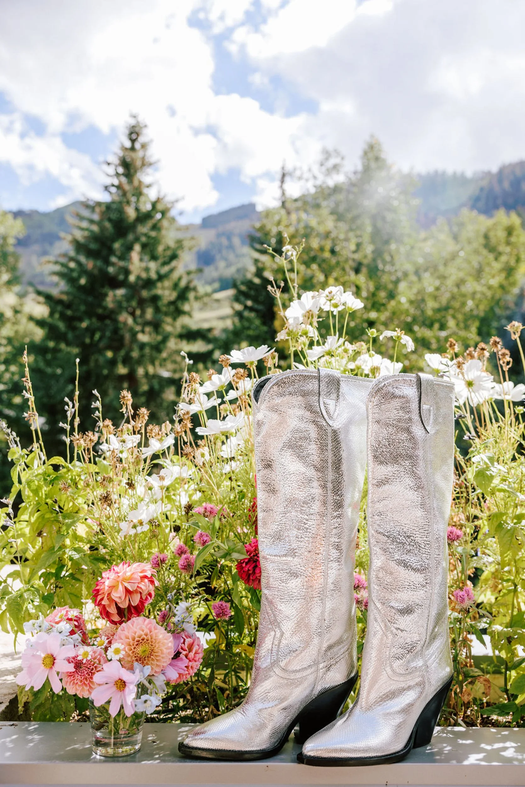 White cowboy boots with pink peony flowers in a summer wildflower meadow with pine trees and mountains, Pine Creek Cookhouse wedding styling detail