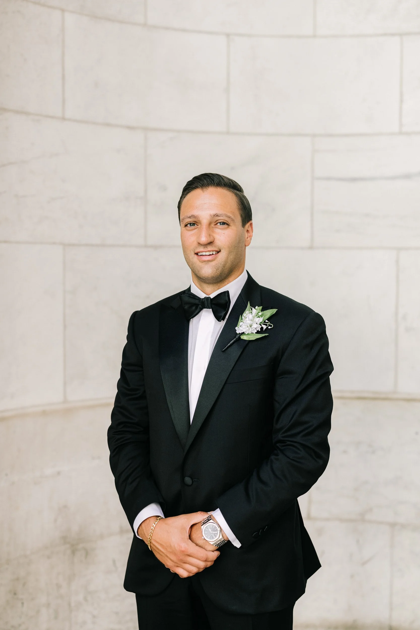 Smiling groom in a dapper black tuxedo in a solo portrait at the New York Public Library, NYC wedding