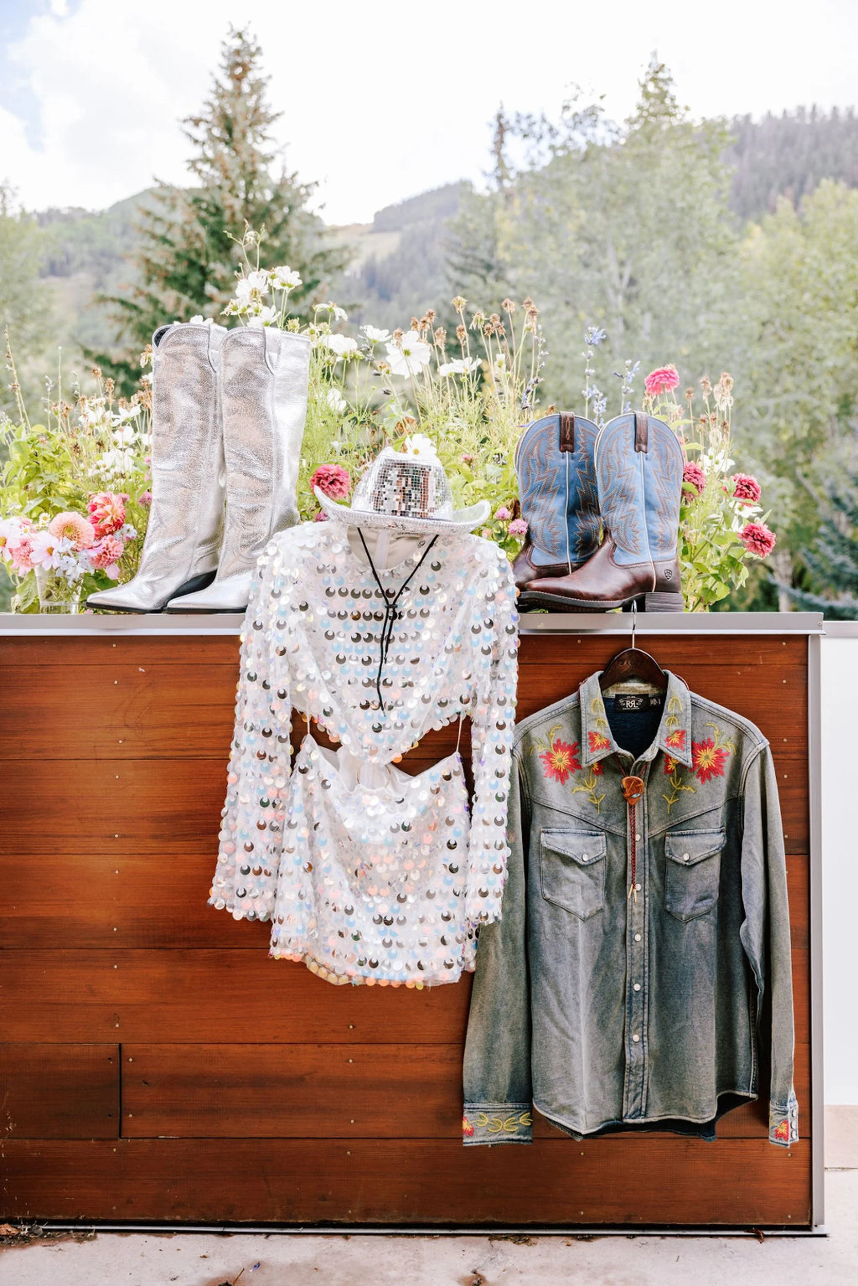 White lace wedding dress and denim western jacket hanging together on wood wall, Pine Creek Cookhouse rodeo disco wedding details