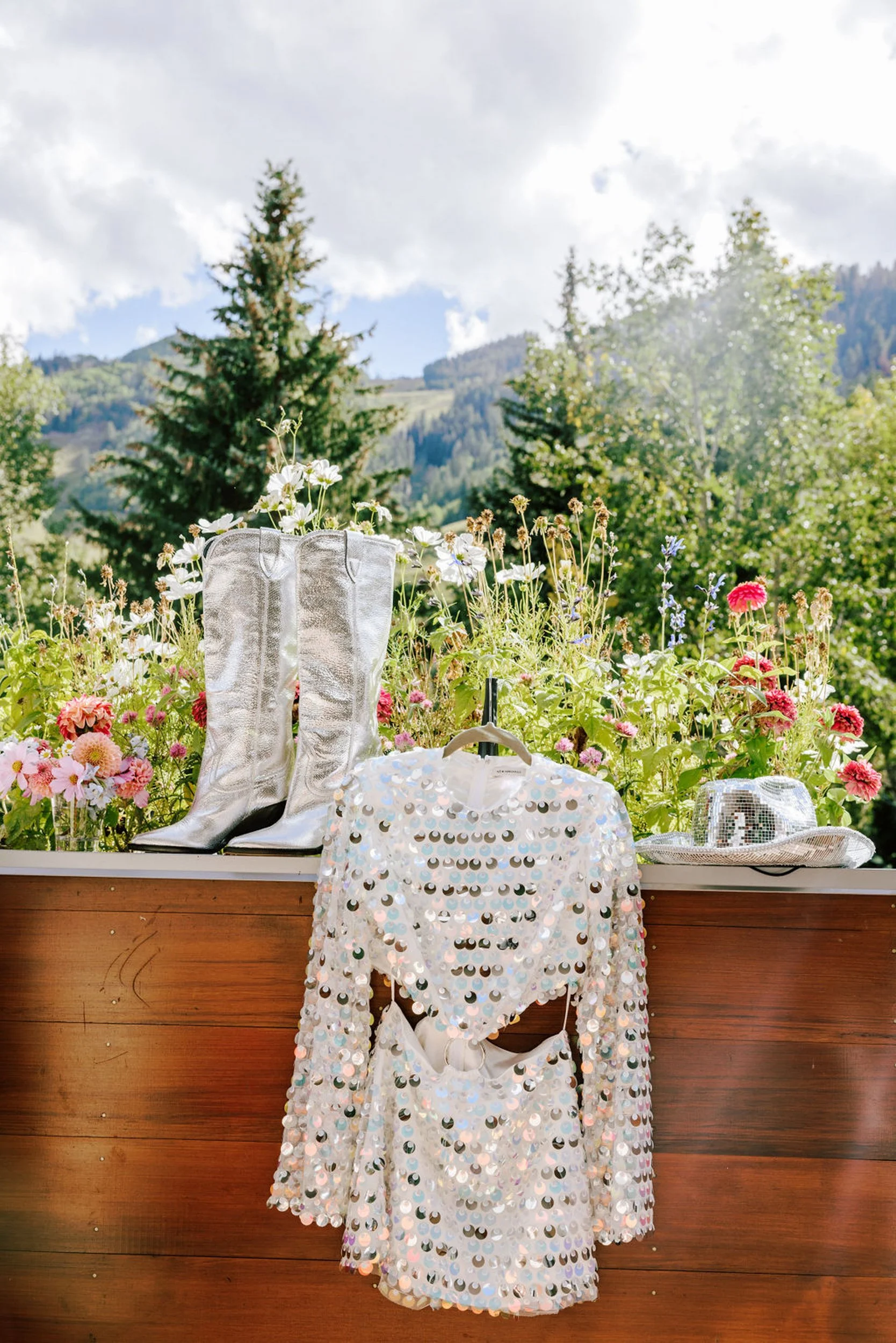 White lace wedding dress and silver cowboy boots displayed with pink wildflowers against a Colorado mountain backdrop, Pine Creek Cookhouse wedding details