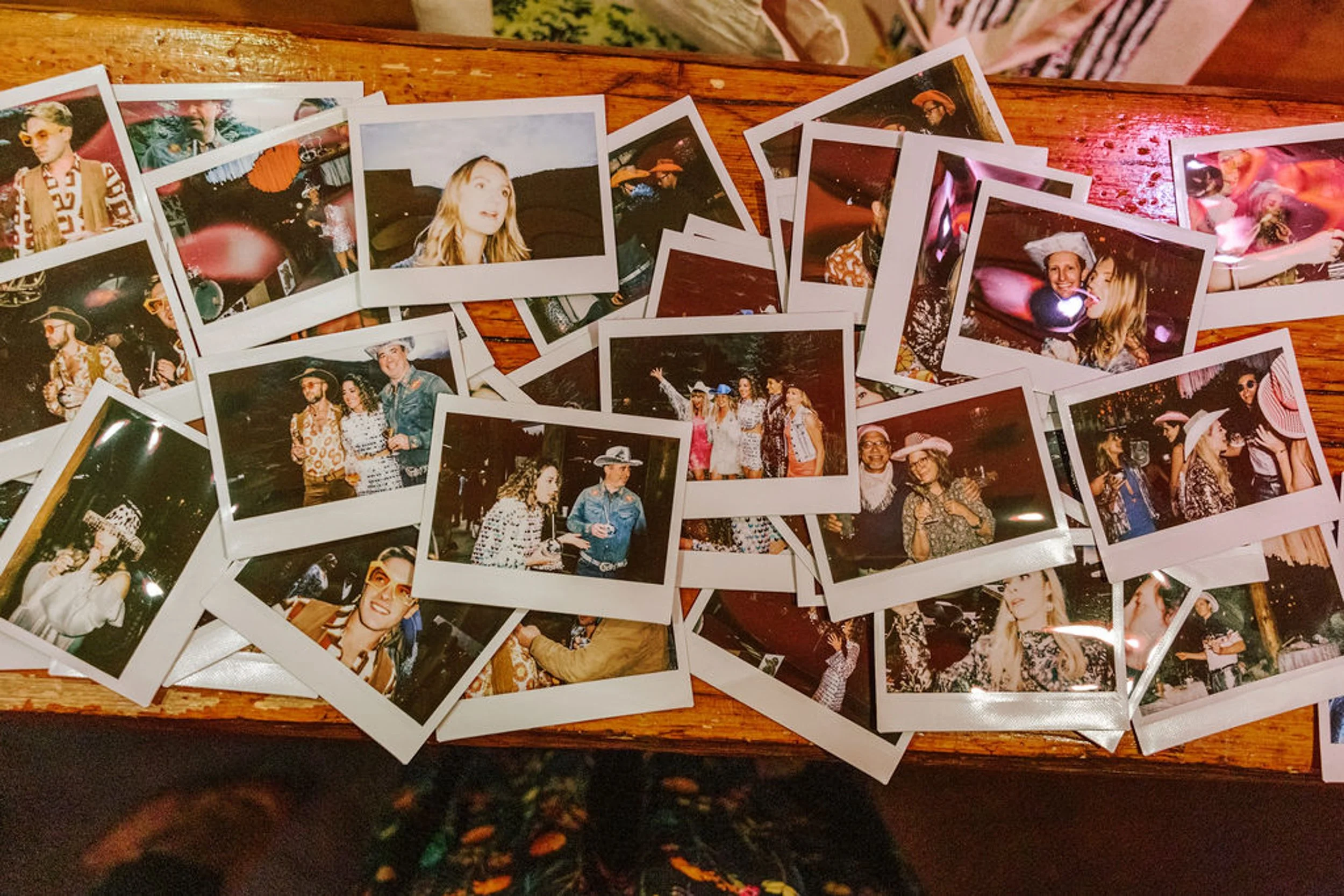 Collection of polaroid photo booth pictures scattered on a wooden table from Pine Creek Cookhouse rodeo disco wedding reception in Colorado