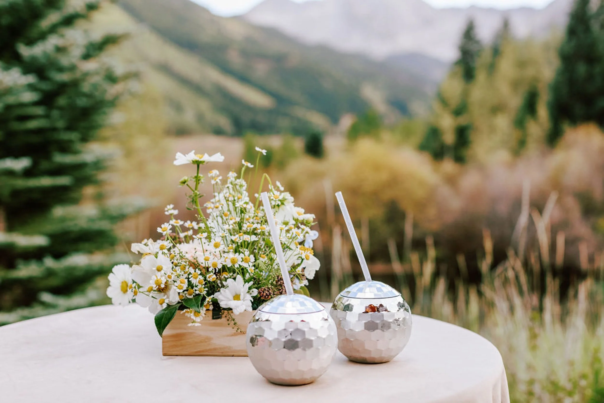 Silver disco ball drinks and wildflower centerpiece on an outdoor reception table at Pine Creek Cookhouse with the Elk Mountains visible behind, rodeo disco wedding detail