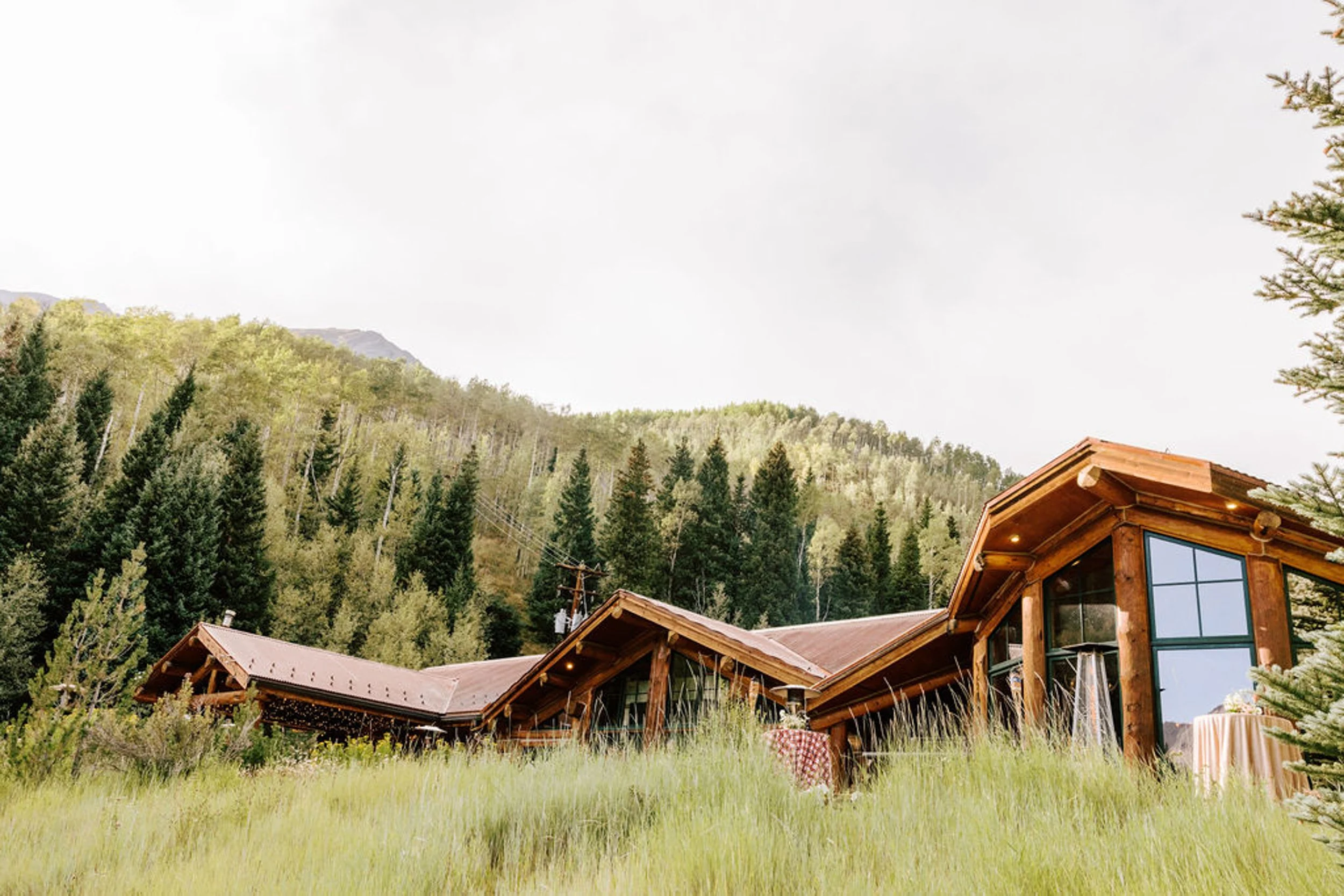Pine Creek Cookhouse nestled in a summer green meadow with the Elk Mountains rising behind it, Ashcroft Colorado wedding venue photography
