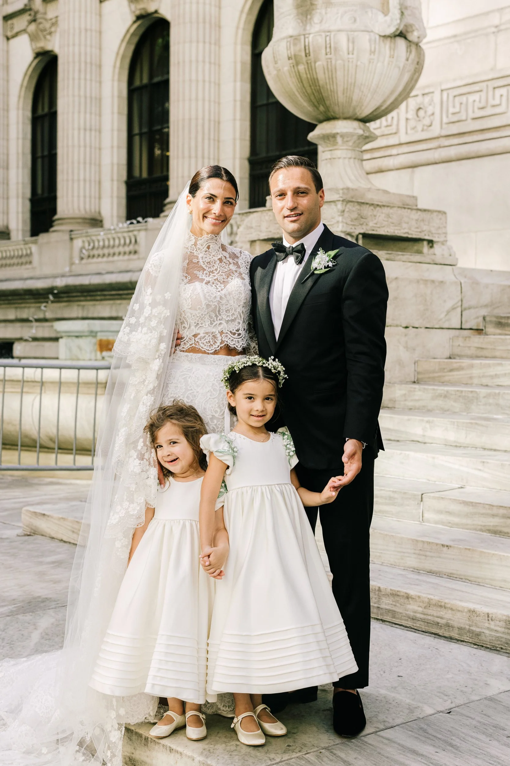 Bride and groom with two flower girls in white dresses in a sweet family portrait at the New York Public Library, NYC wedding