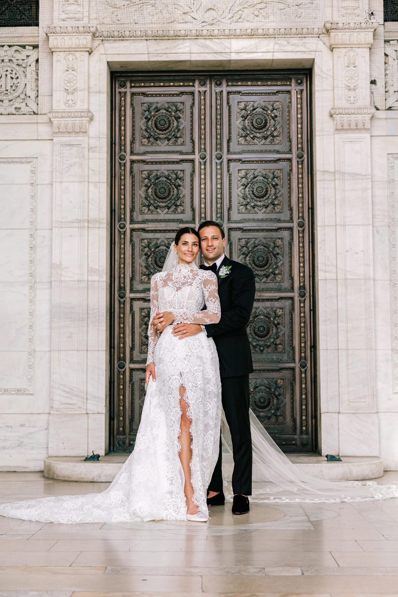 Bride and groom embracing in front of the grand bronze doors of the New York Public Library entrance, NYC wedding