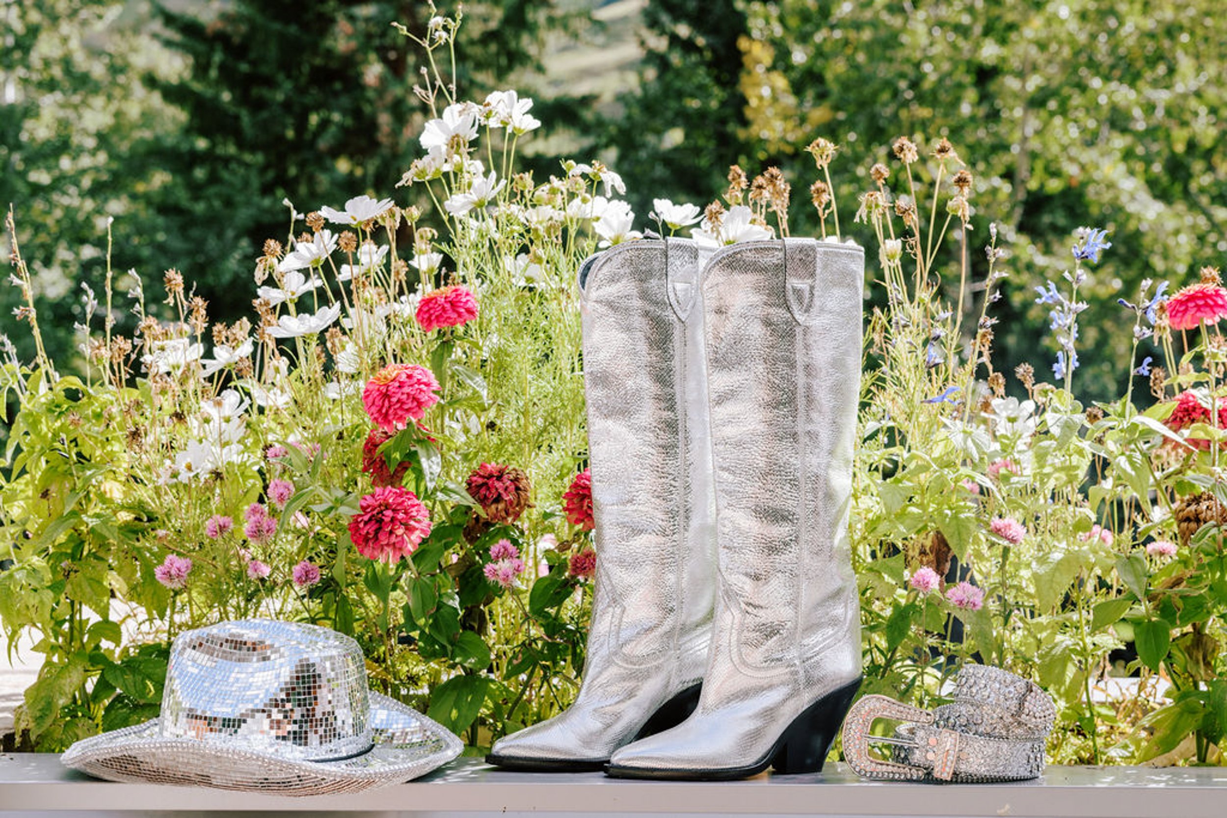 Silver white cowboy boots and hat displayed in a pink wildflower meadow, wedding detail photography at Pine Creek Cookhouse Aspen Colorado
