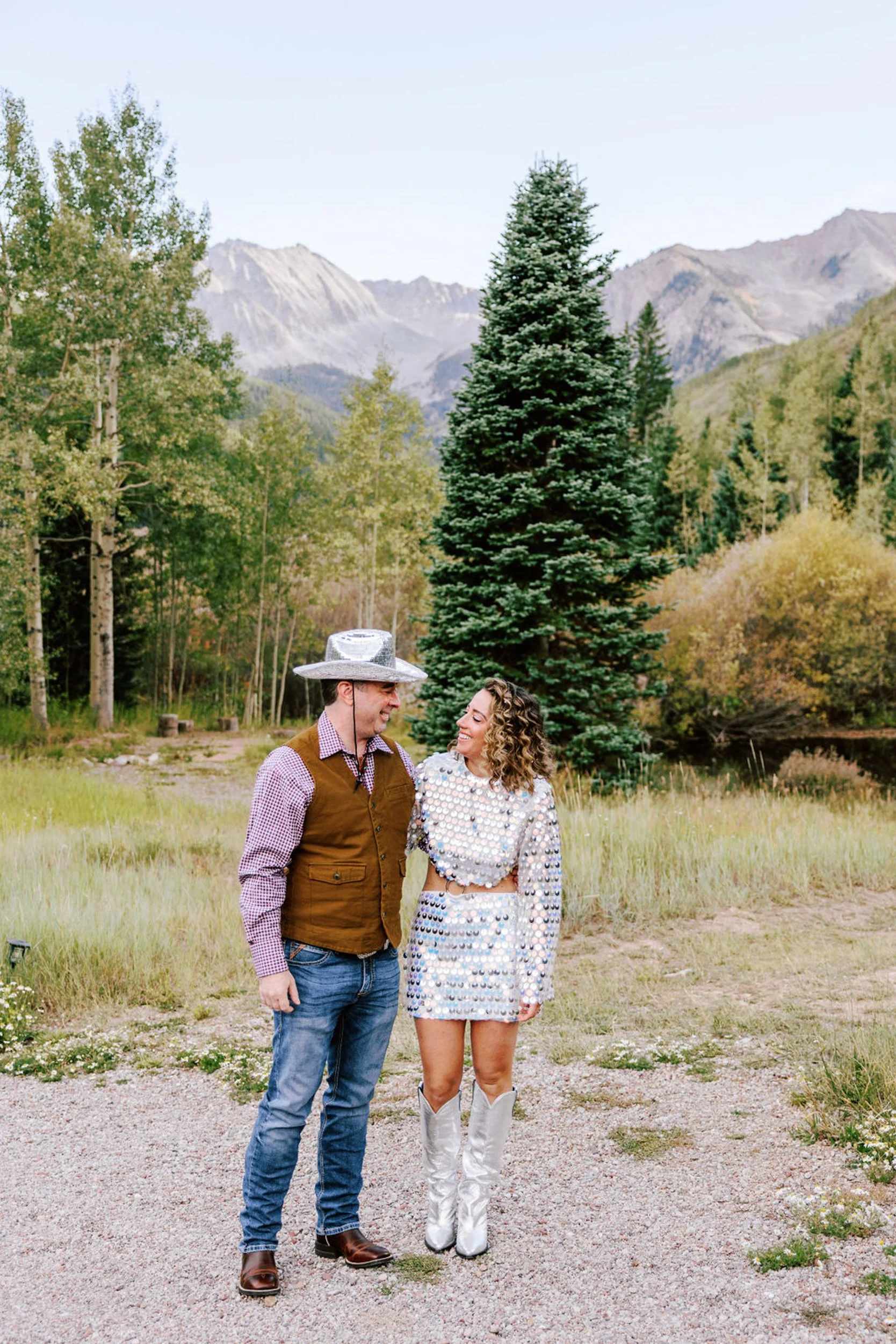 Bride in white cowboy boots and groom in western vest and hat standing on mountain path at Pine Creek Cookhouse, Castle Creek Valley Aspen area wedding