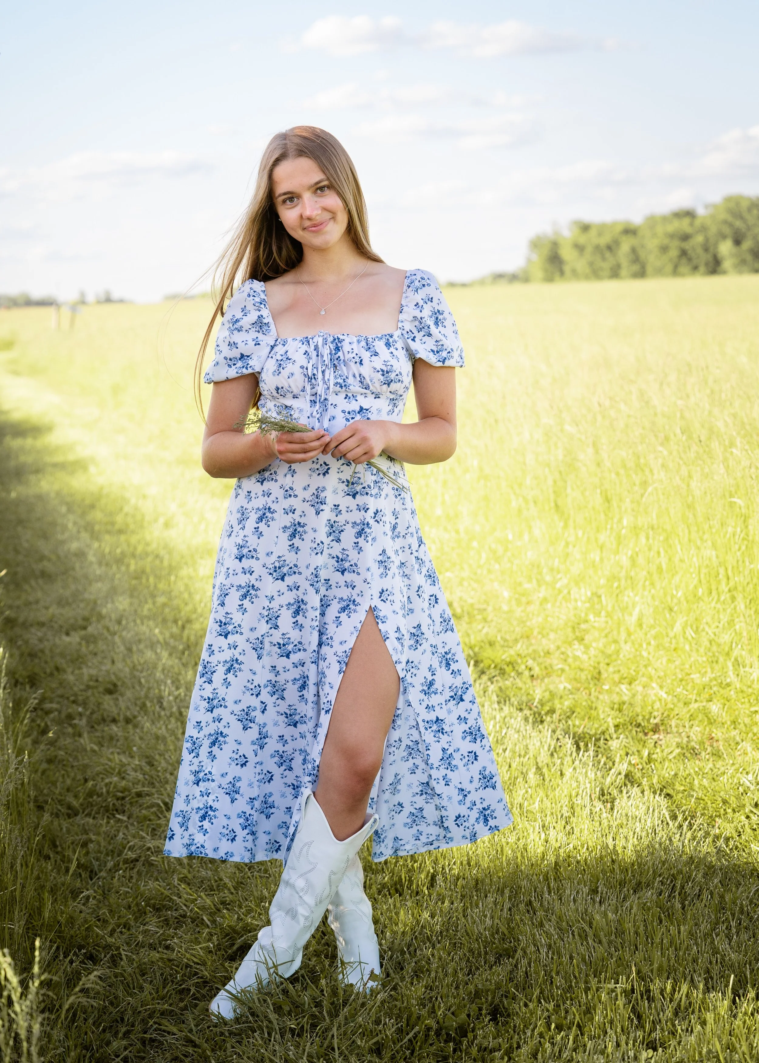 senior girl with blue floral dress in field in white cowboy boots