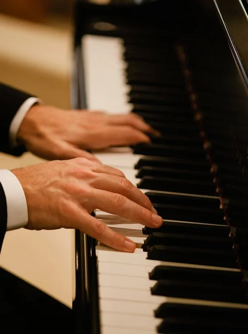Close-up of a person playing a black grand piano with hands on the keyboard.