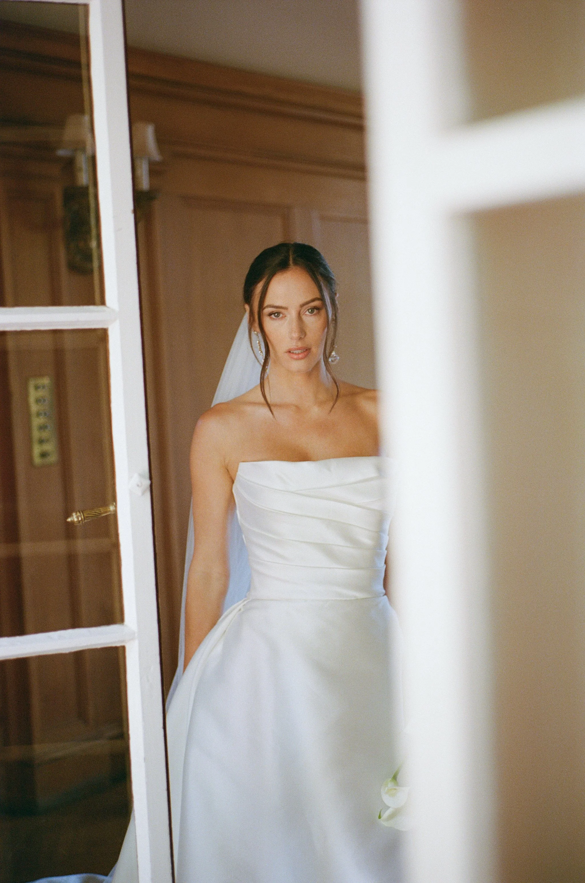 A woman in a white wedding dress and veil is looking at herself in a mirror.