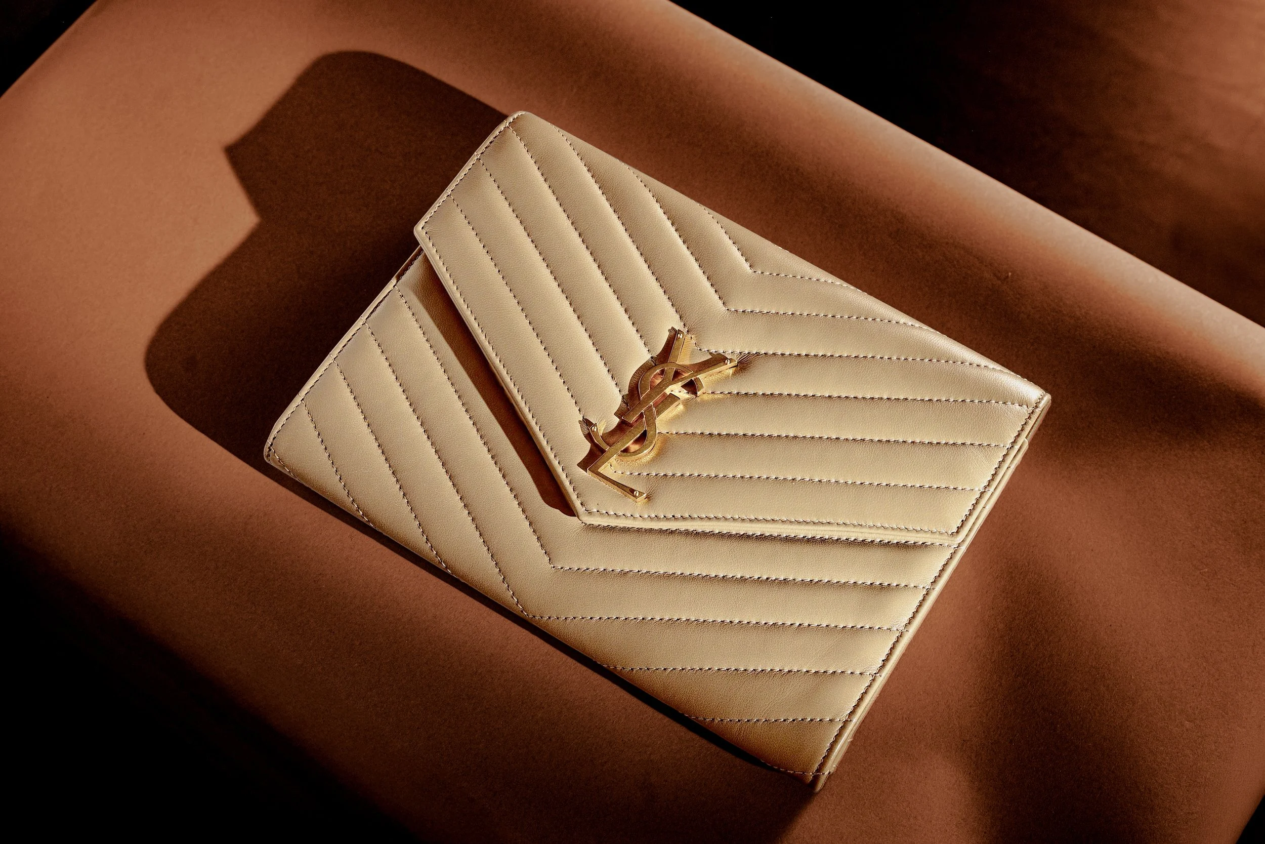 A beige leather YSL clutch with chevron stitching and gold logo on a brown surface.