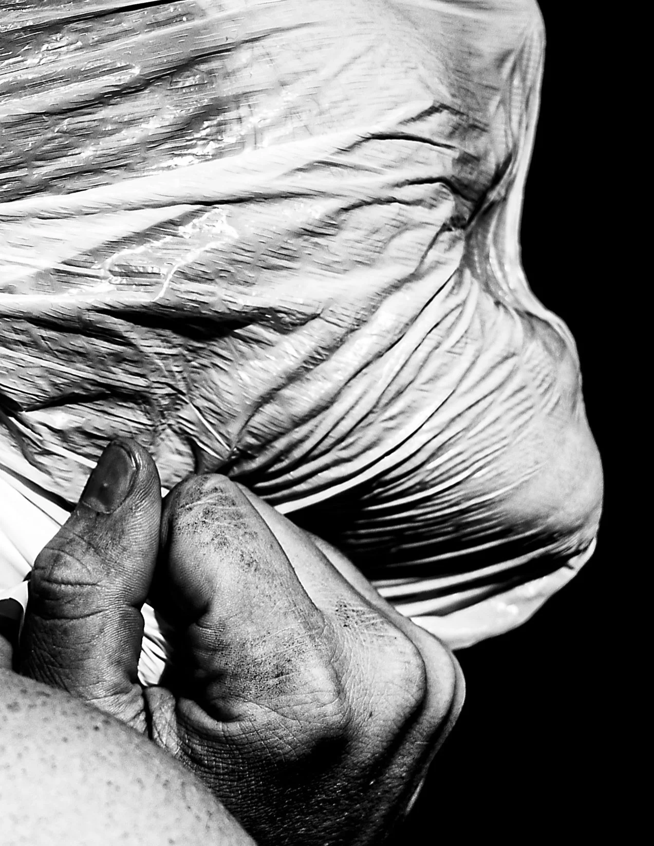 Close-up of a person's hand gripping a wrinkled plastic bag filled with an unknown substance, in black and white.