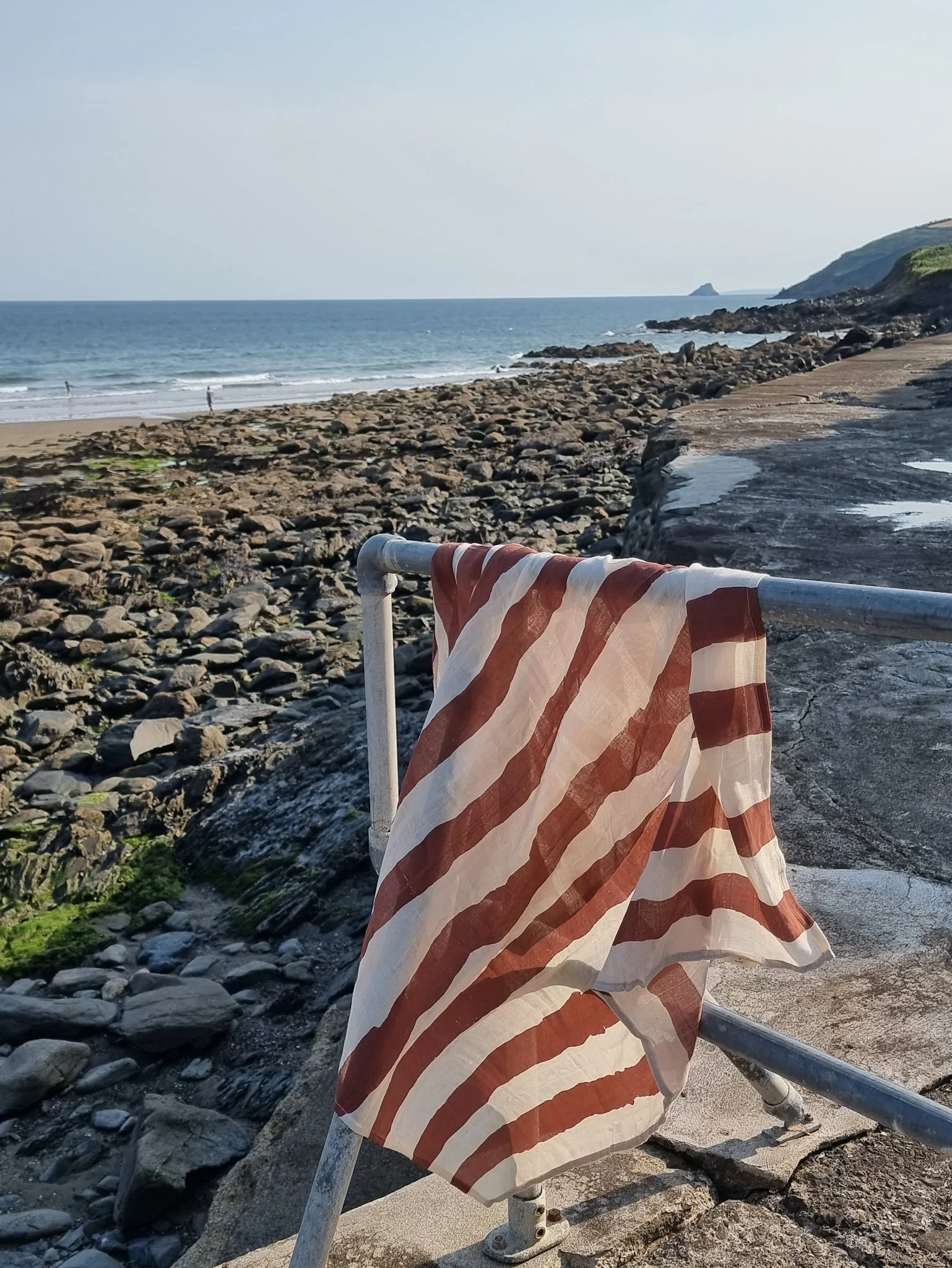 Beautiful muslin blanket, rwsting on a fence, with the sea behind. You can tell that the wind is blowing it.