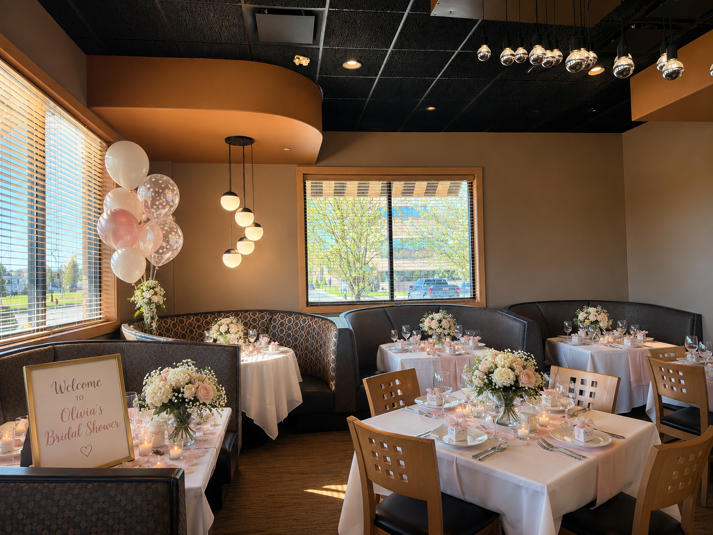 Beautifully decorated interior of a wedding reception with round tables covered in white tablecloths, adorned with pink and white floral centerpieces, candles, and place settings. There are black and wooden chairs, a corner with a cushioned bench, an