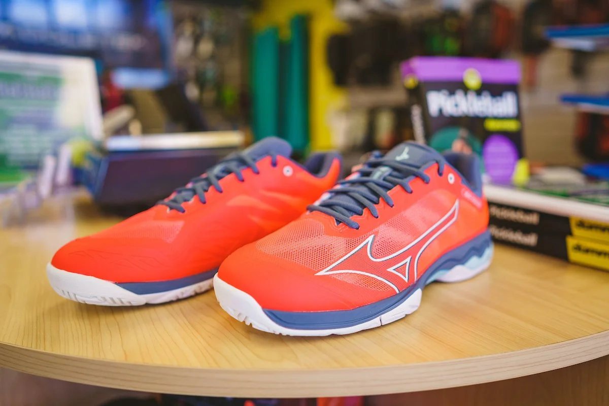 A pair of red and navy running shoes with white soles placed on a wooden surface in a store setting.