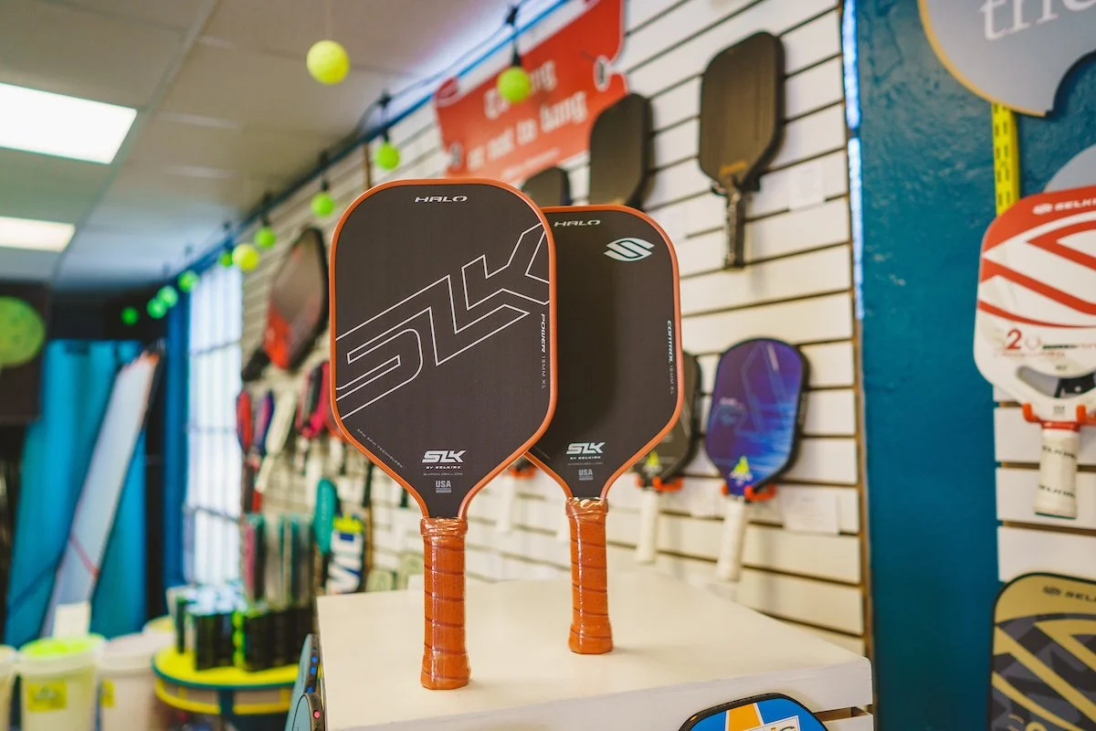 Two pickleball paddles with black and orange design displayed on a white surface inside a sporting goods store.