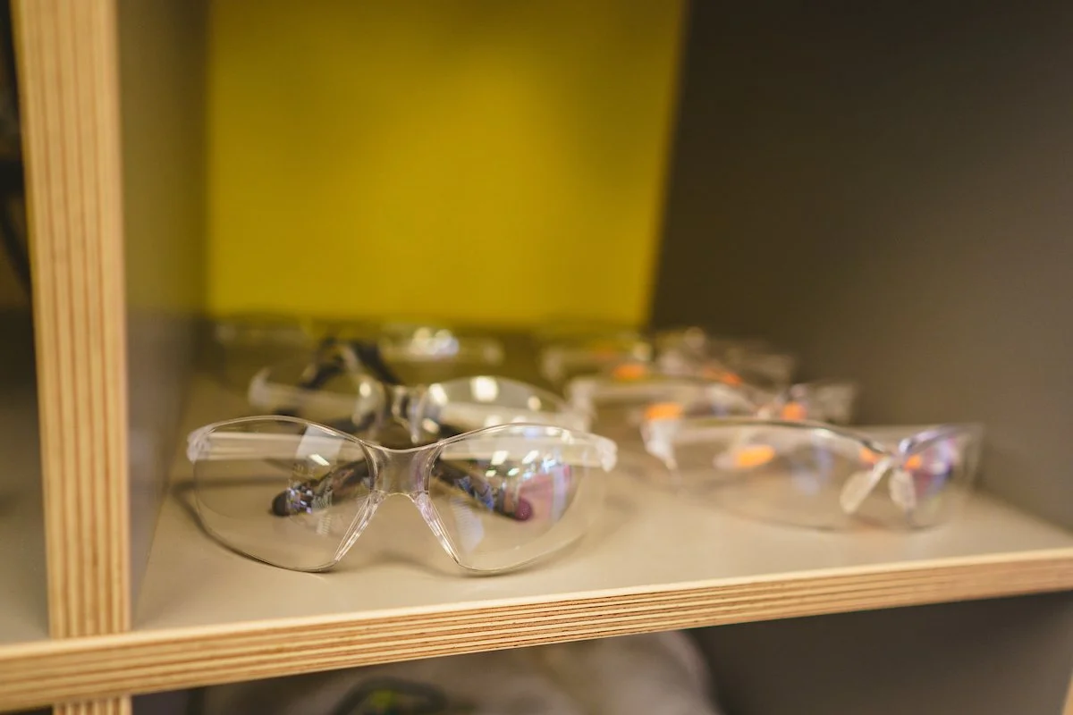 A shelf displaying several pairs of safety glasses, with some glasses having clear lenses and others having tinted or orange lenses.