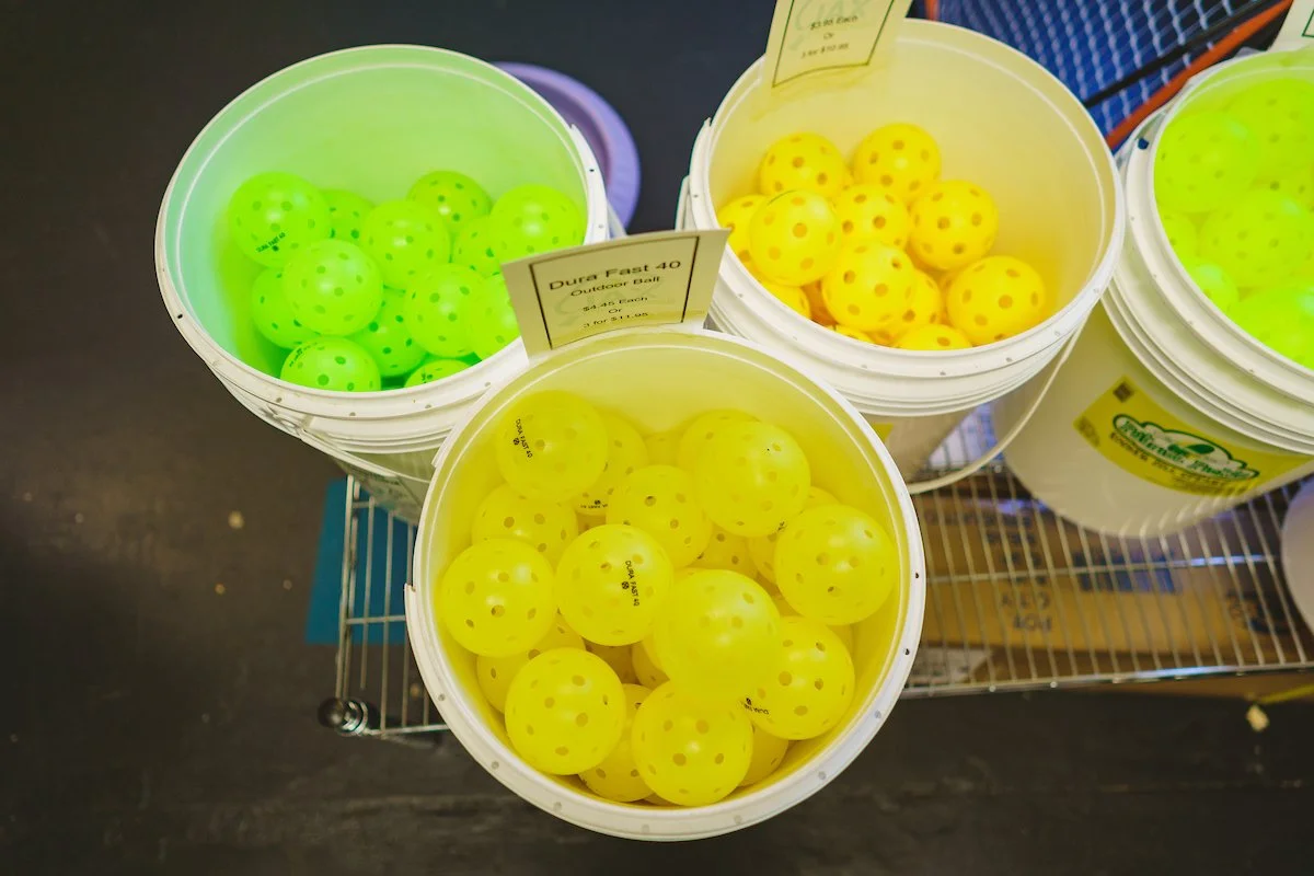 Colorful buckets of plastic golf balls in green, yellow, and yellow with red dots, displayed on a metal shelf at a sporting goods store.