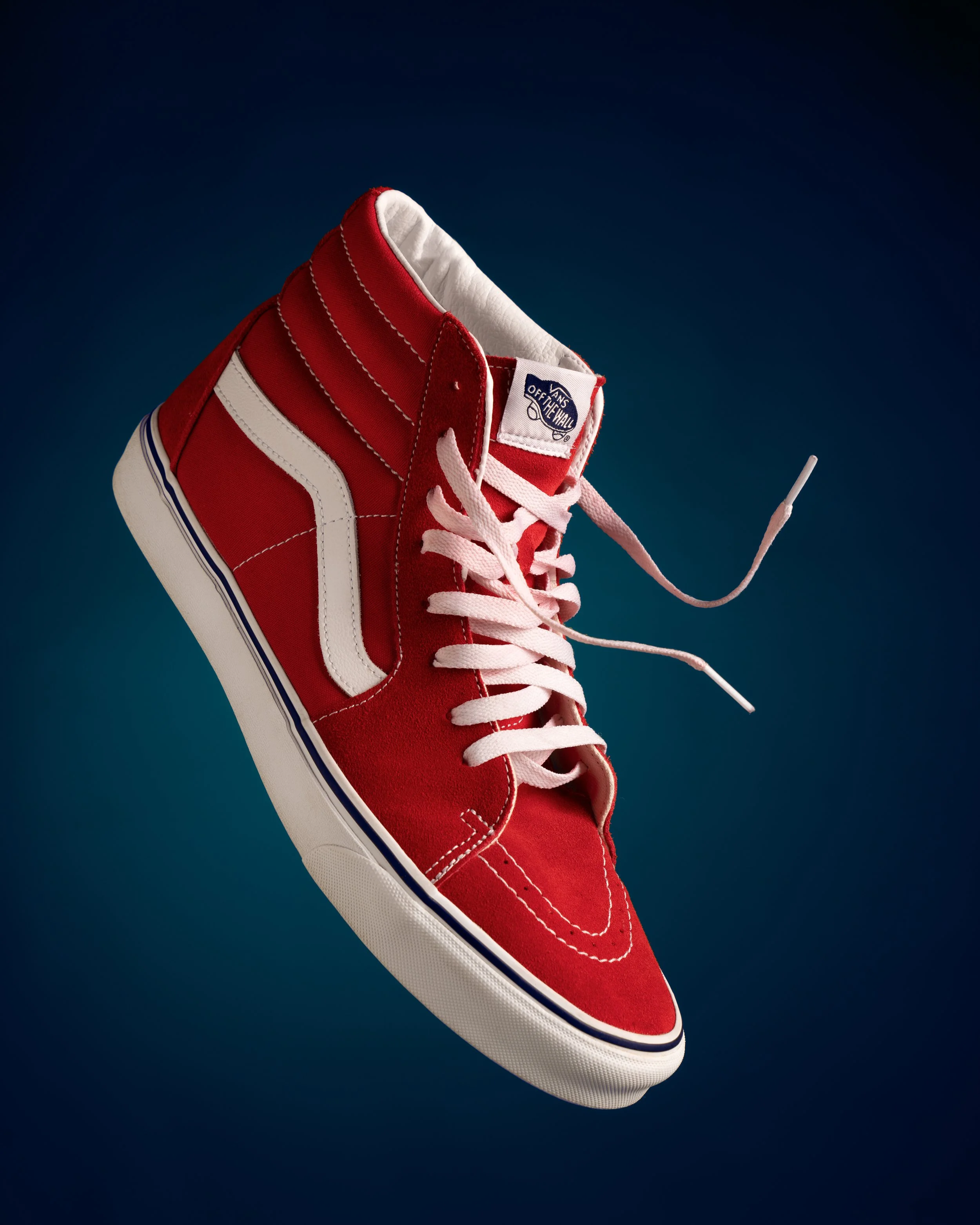 A red Vans sneakers with white accents is floating against a blue background.