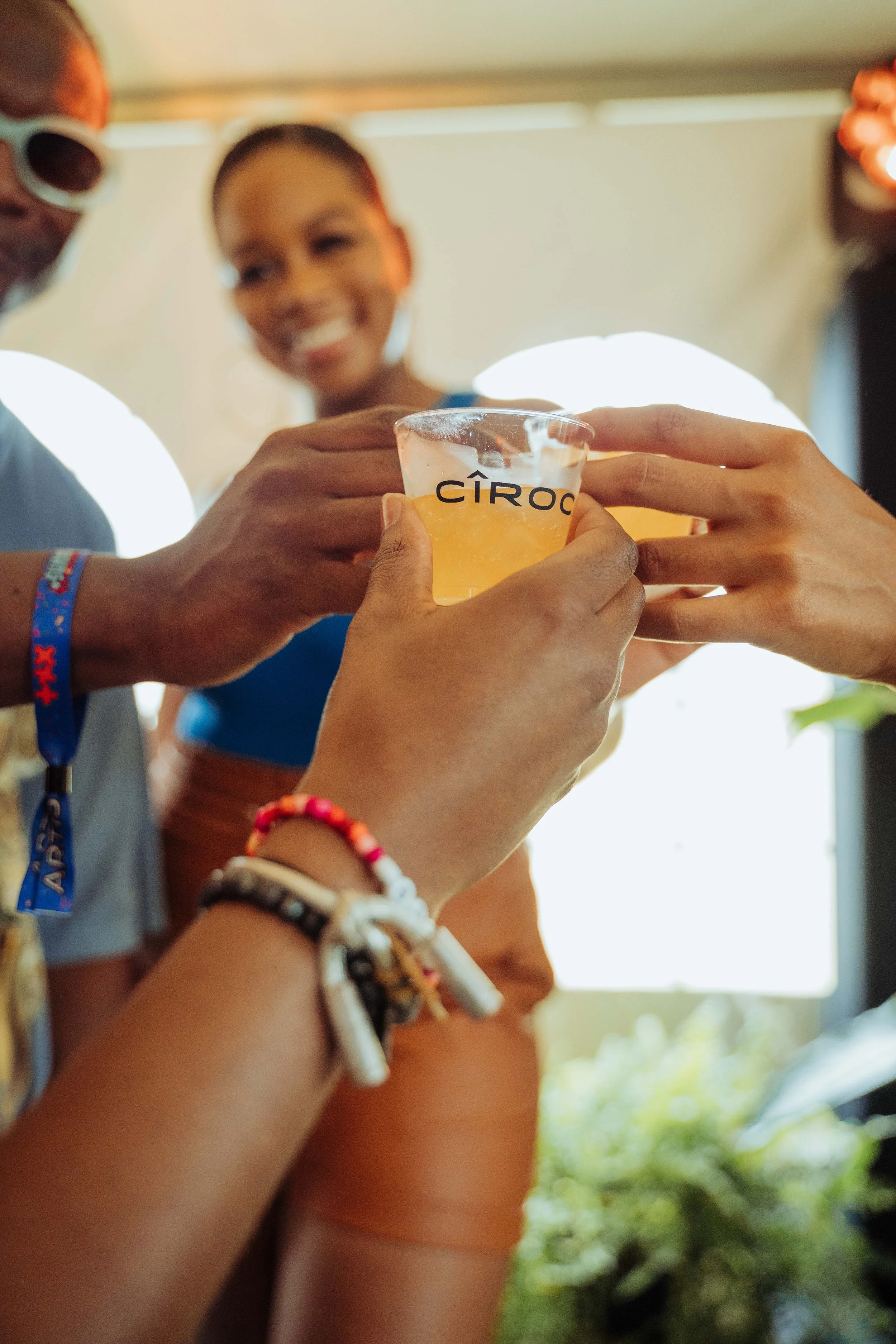 People clinking glasses during a celebration, with one glass labeled 'CÎROC' visible in the center, and smiling individuals in the background.