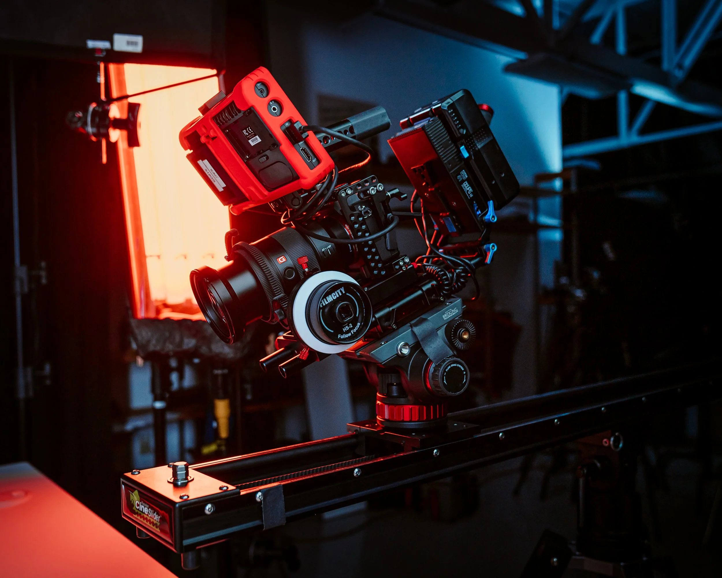 A professional camera mounted on a rail system with red and blue lighting, used for film or television production.