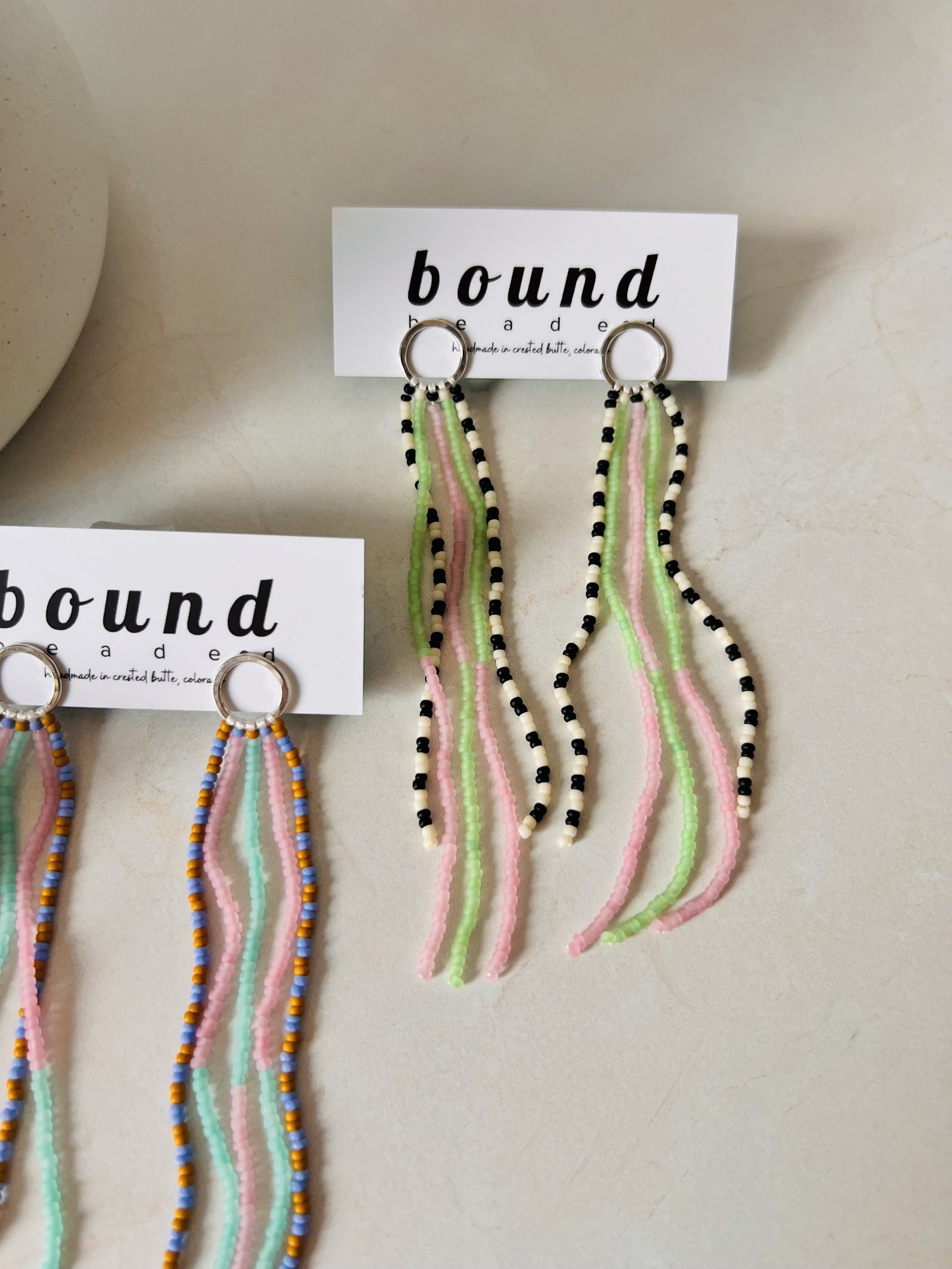 Beaded color earrings with black, white, green, and pink beads on white cards labeled 'bound'.