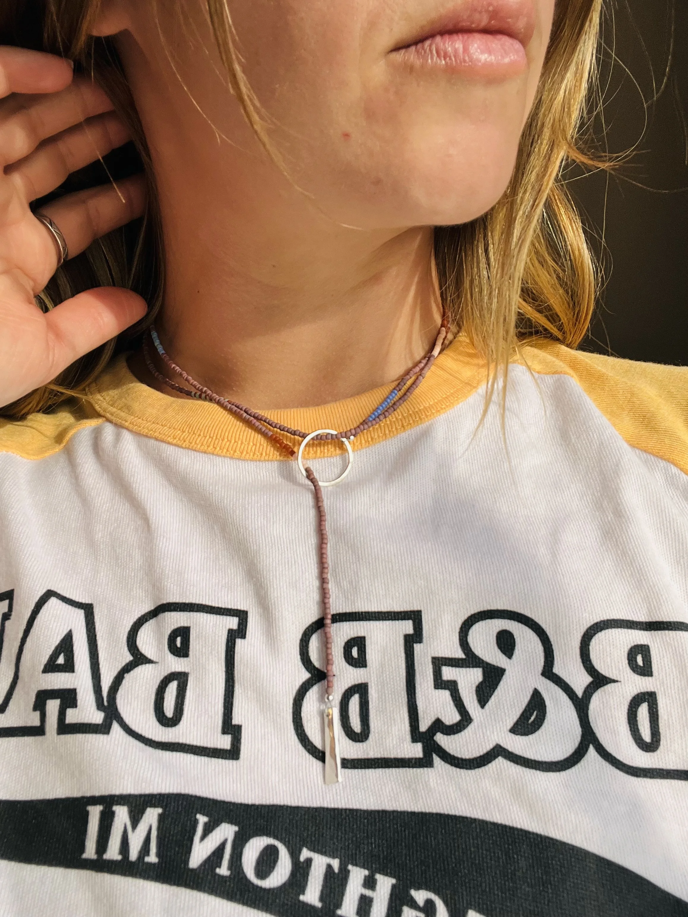 Close-up of a person wearing a layered beaded necklace with a circular ring pendant and a casual t-shirt with text on it.