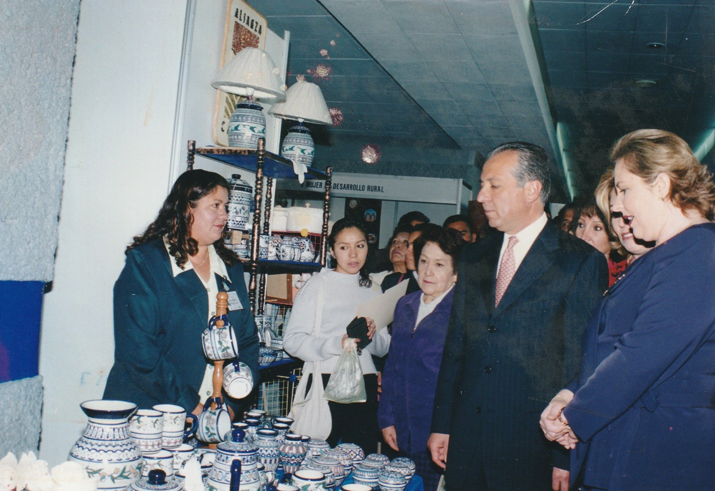 Grupo de personas visitando una feria de artesanías con piezas de cerámica decoradas con patrones azules y blancos.