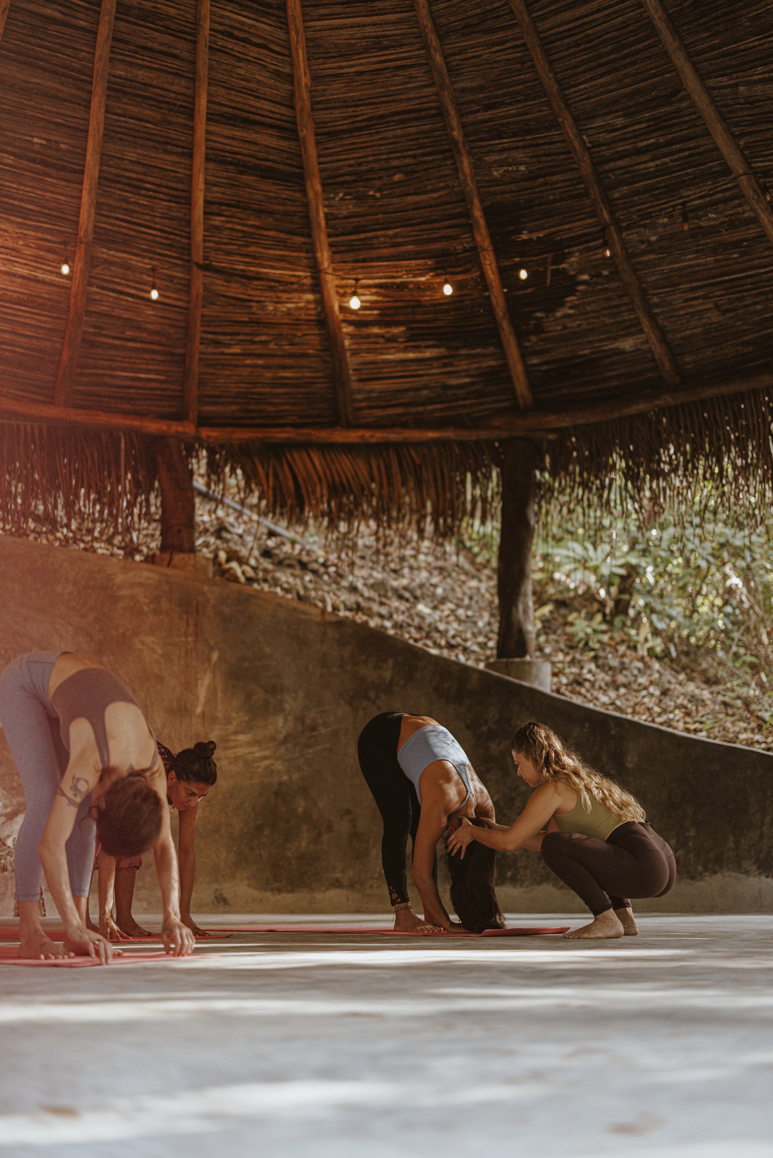 Group of women practicing yoga in an open-air bamboo hut with natural surroundings.