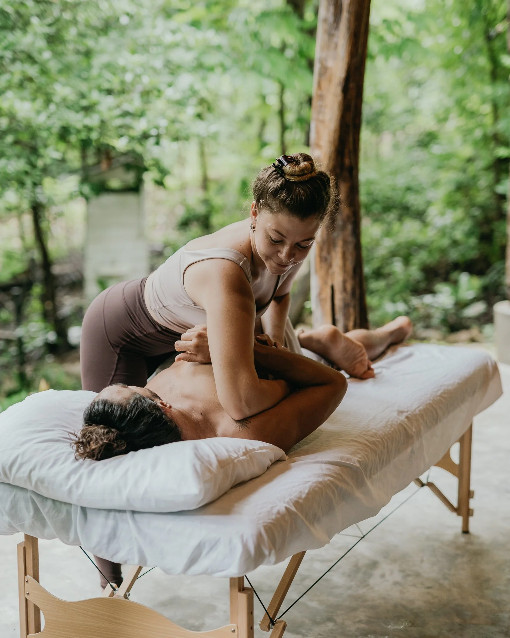 A woman receiving a massage outdoors on a massage table in a forest setting.