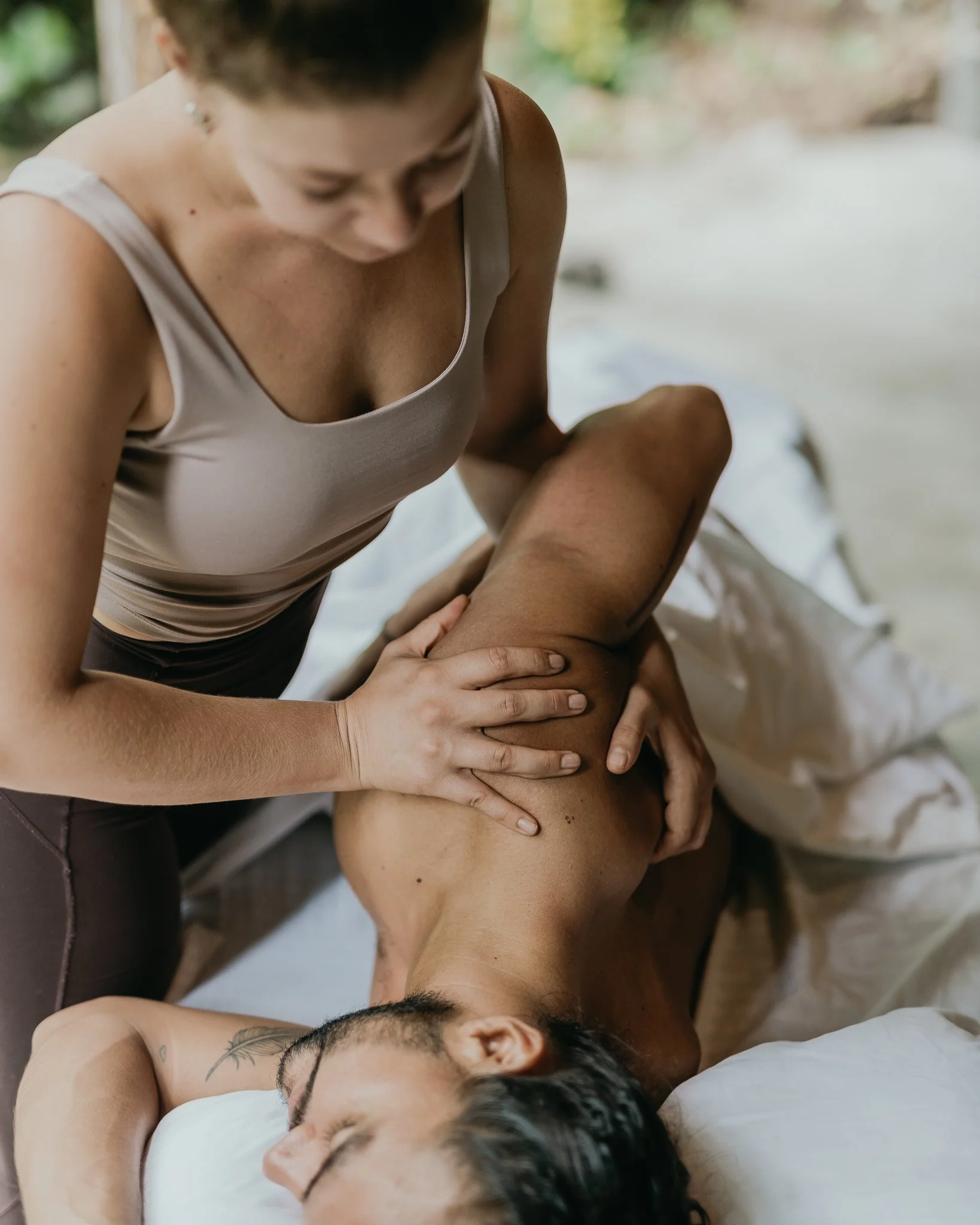 Woman giving a massage to a person lying on a bed outdoors.
