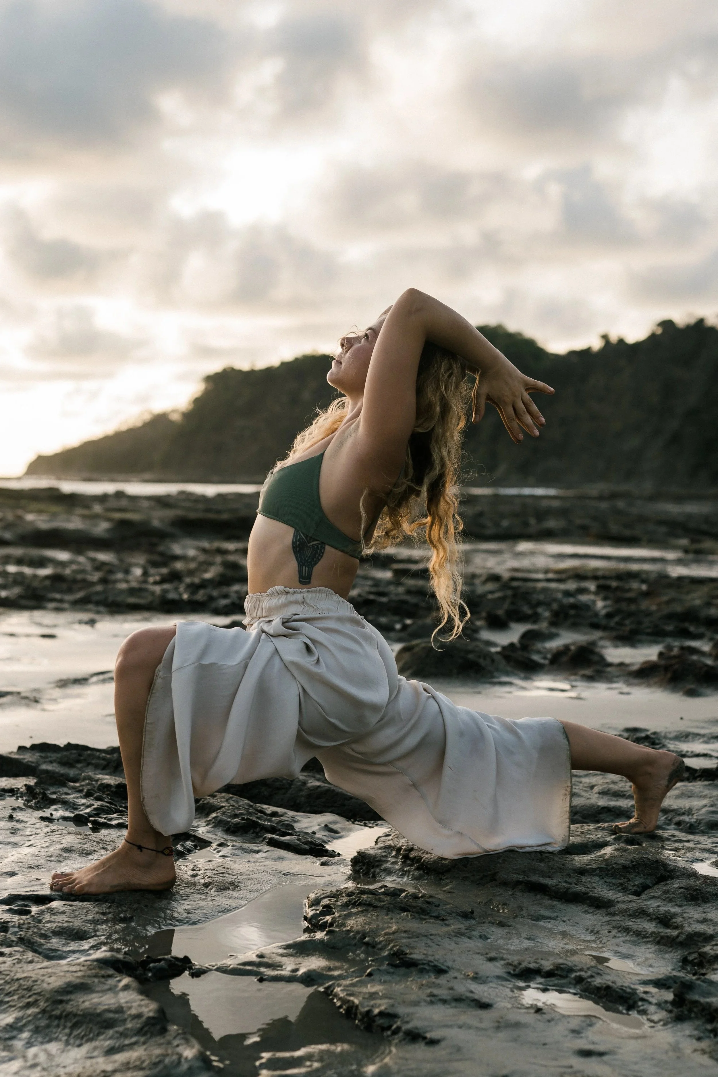 Woman practicing yoga outdoors on rocky terrain near the coast during sunset.
