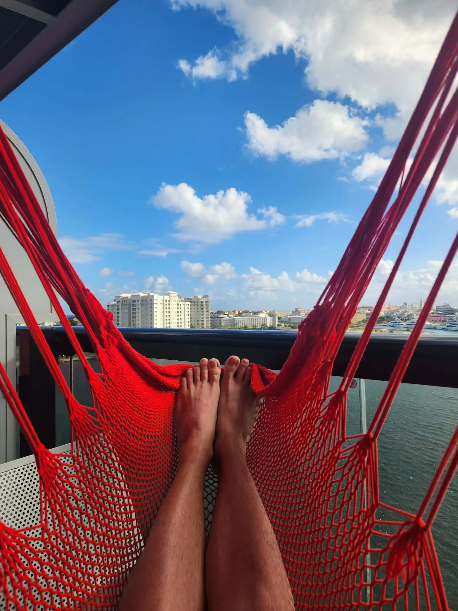 red hammock with feet poking out and overlooking the ocean and a large white resort building