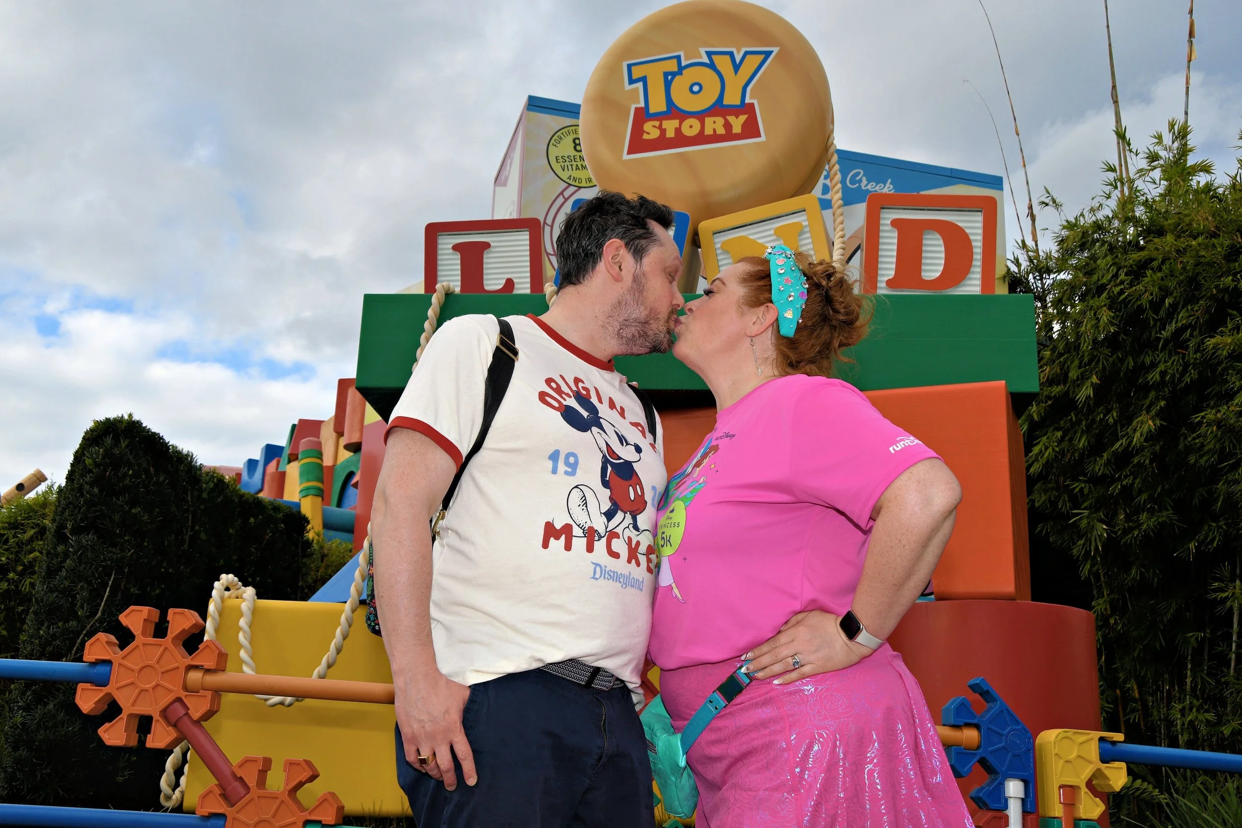 Noddea and her husband sharing a kiss in front of the Toy Story Land sign during a runDisney race weekend.