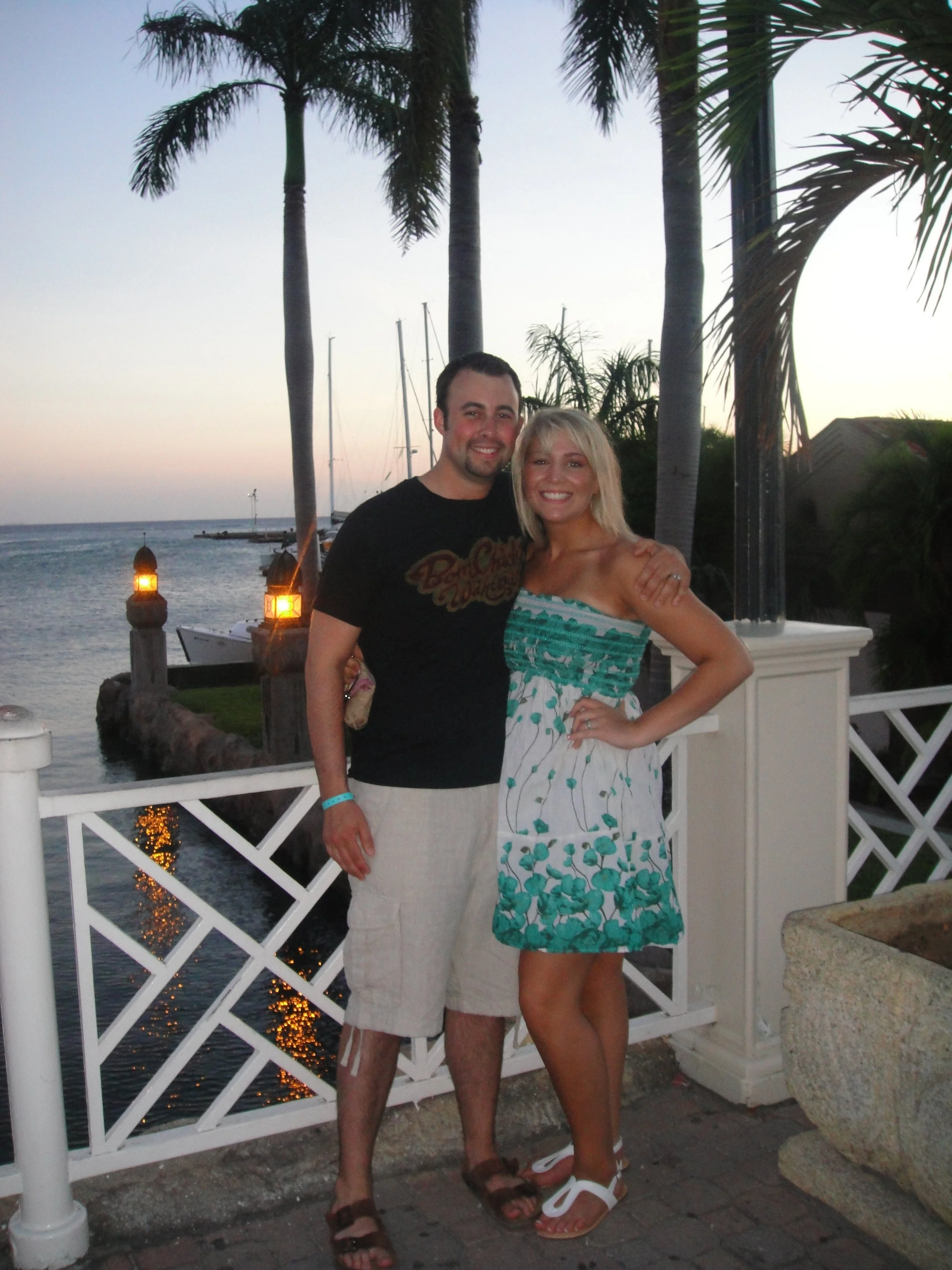 JPGCouple embracing at sunset on a waterfront balcony lined with palm trees.
