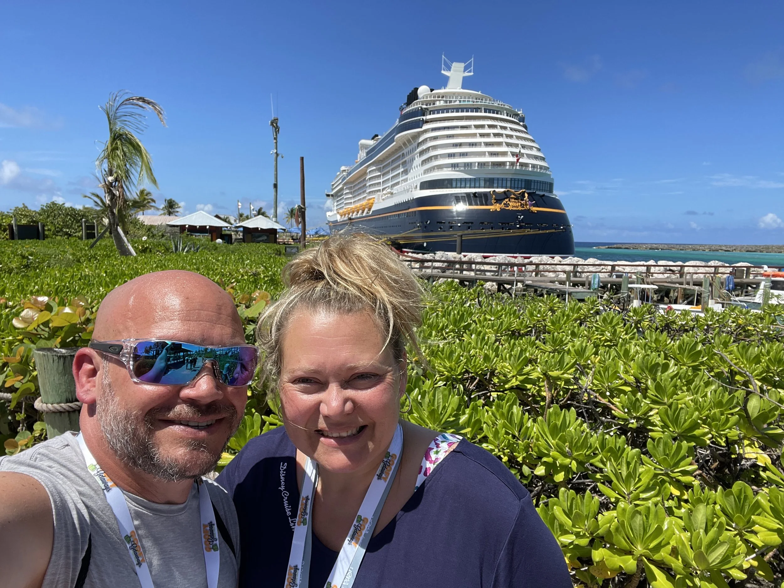 a man and woman smiling with a cruise ship in the background