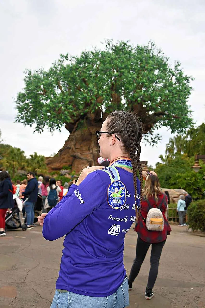 A runner wearing her finisher medal and race shirt looks up at the Tree of Life in Disney's Animal Kingdom after finishing a race.