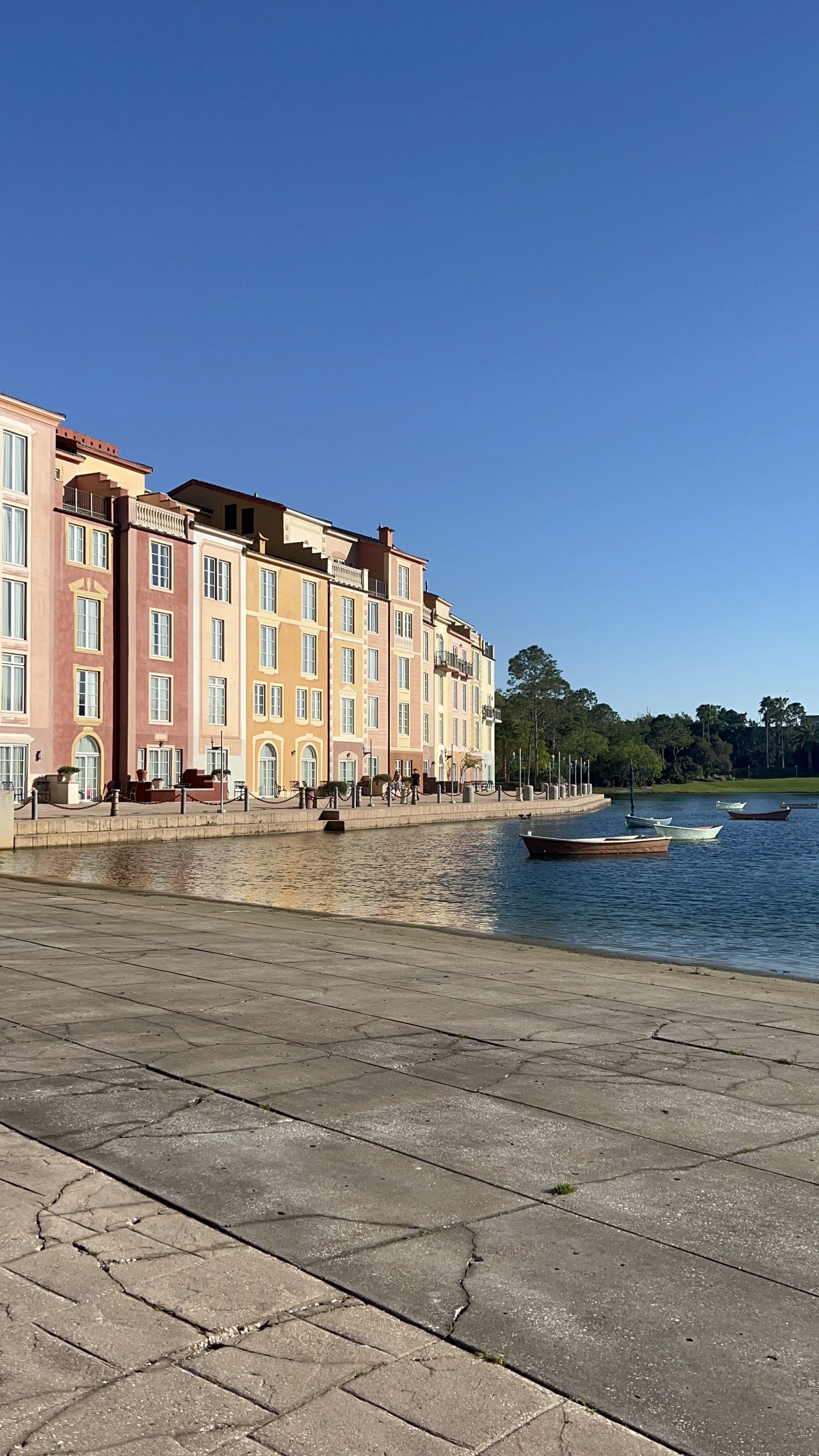 Mediterranean-style resort buildings and docked boats along a lagoon at a Universal Orlando on-property resort under a clear blue sky.
