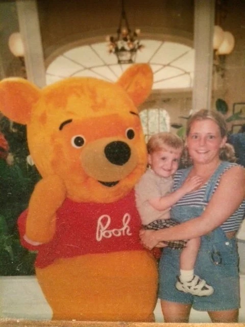 An early family photo of a young Aly holding her son next to Winnie the Pooh.
