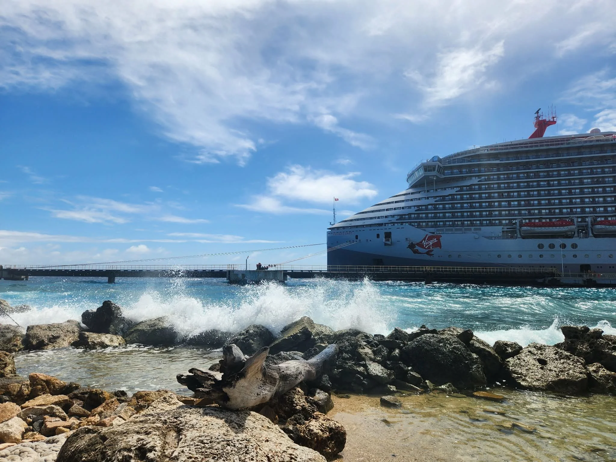 virgin voyages ship docked at port with ocean waves and rocks